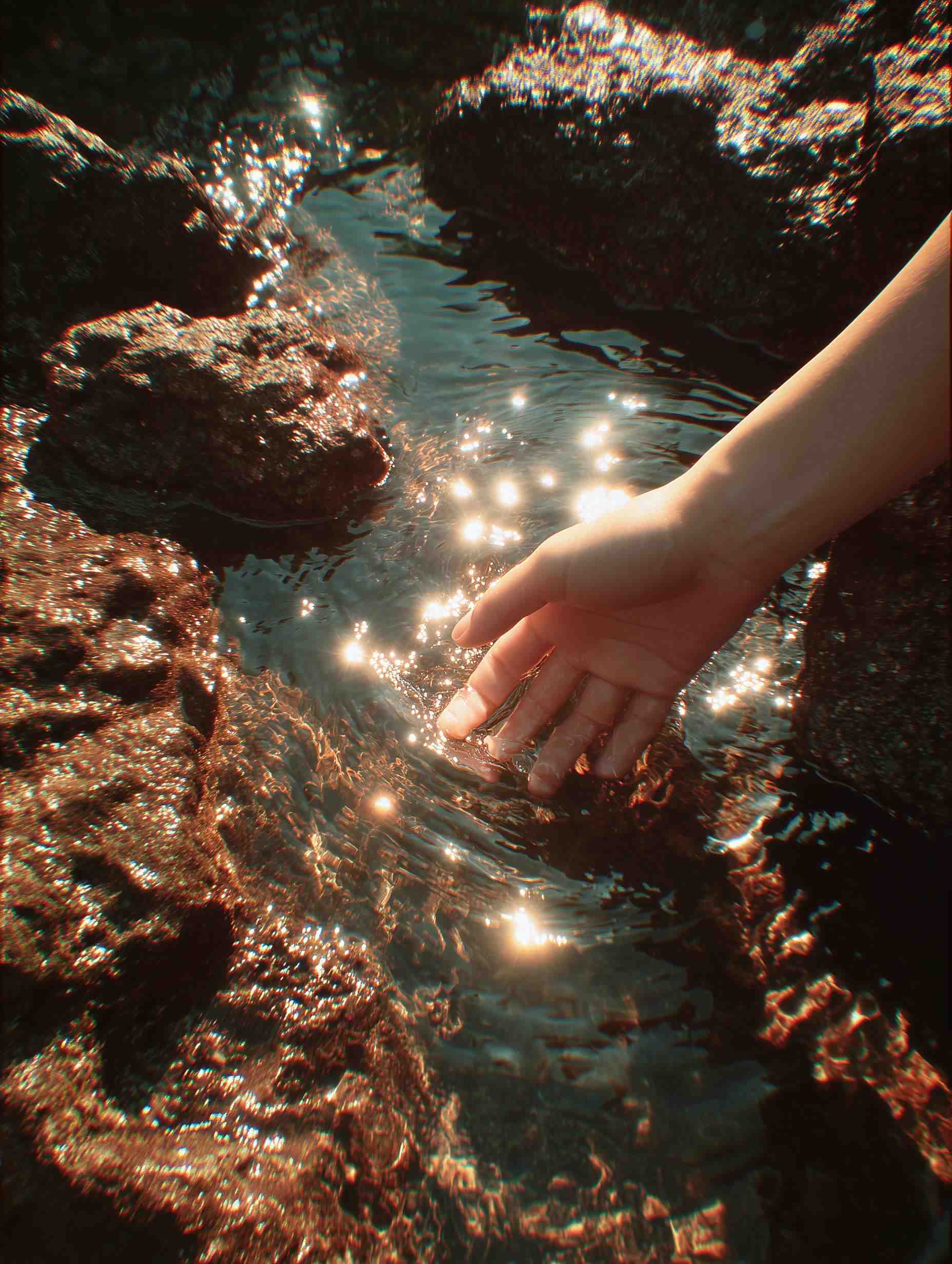 Hand touching glowing turquoise water near dark rocks