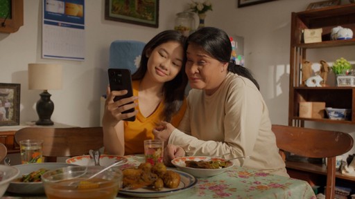 Mother and daughter sharing moment while using phone during dinner in cinematic brand film for DCOM Money Express, produced by Visual Producer Indonesia