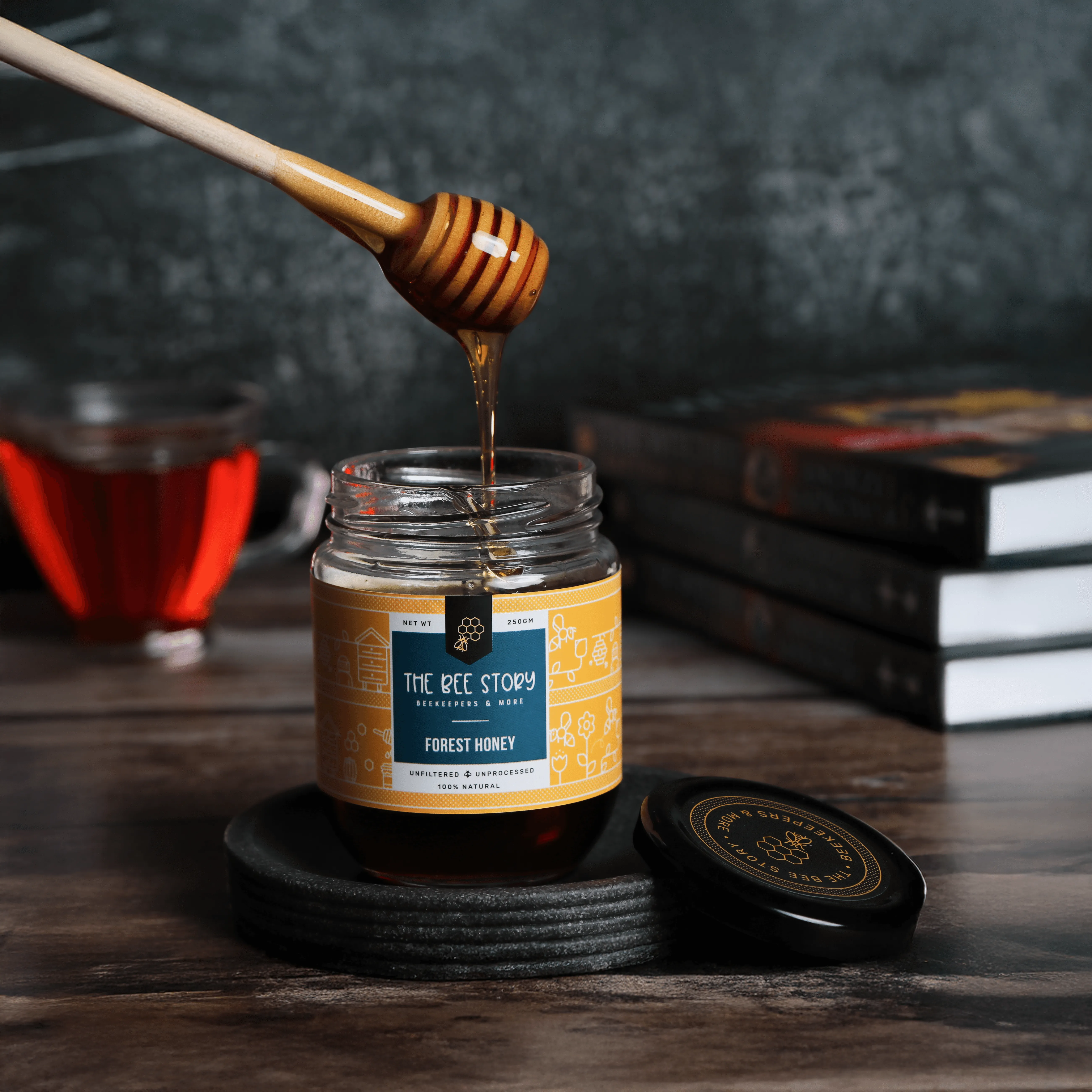 A jar of honey on a wooden table with a honey dipper drizzling honey, surrounded by books.