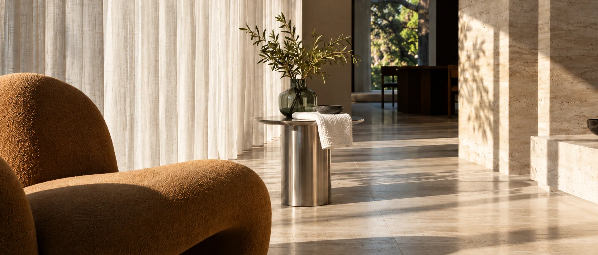 AI-generated illustrative sunlit interior with a caramel chair, linen curtain and stone surfaces.