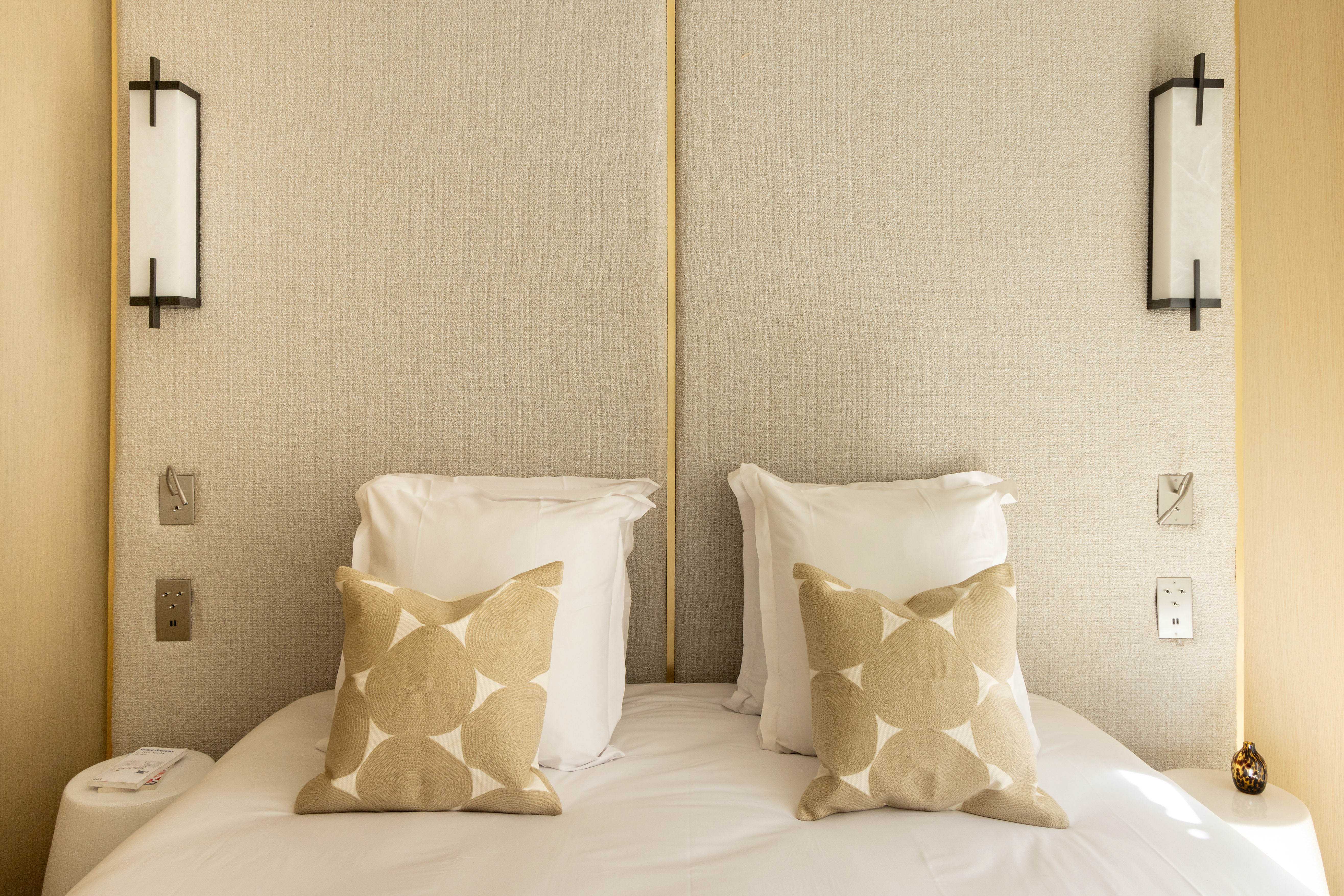 Tete de lit tissee beige avec coussins graphiques dores, appliques murales noires et interrupteurs dores