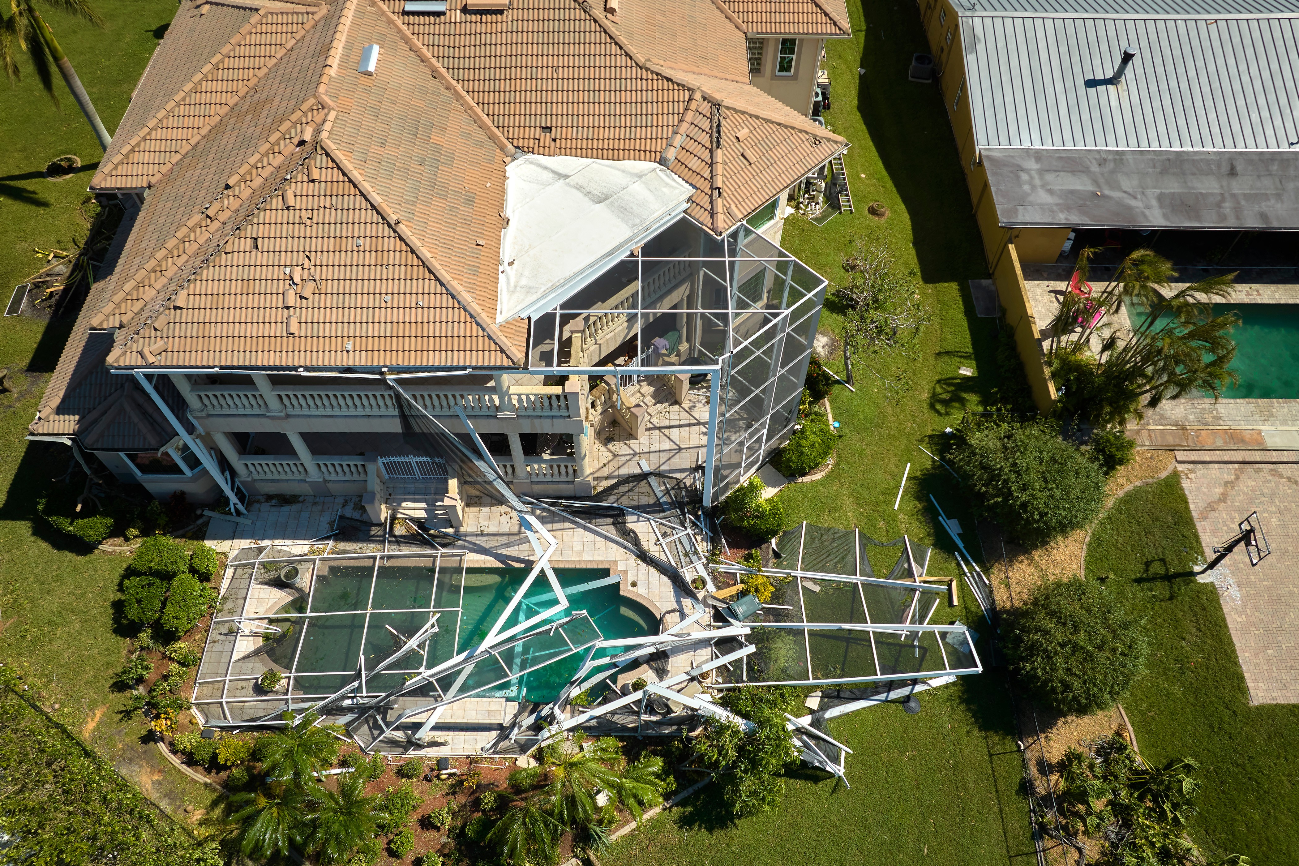 Overhead view of a Tampa home with severe hurricane damage to pool enclosure and lanai, showing collapsed aluminum frames and torn screens