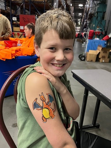 Smiling boy with Charizard shoulder face paint sitting in a warehouse setting