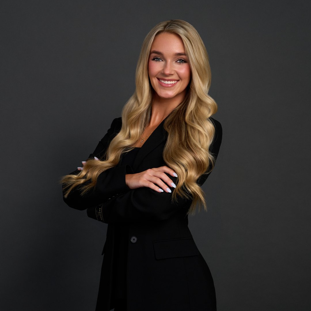 A young man with glasses and a denim shirt sits confidently against a blue wall. Art and cacti decorate the space, conveying a creative vibe.
