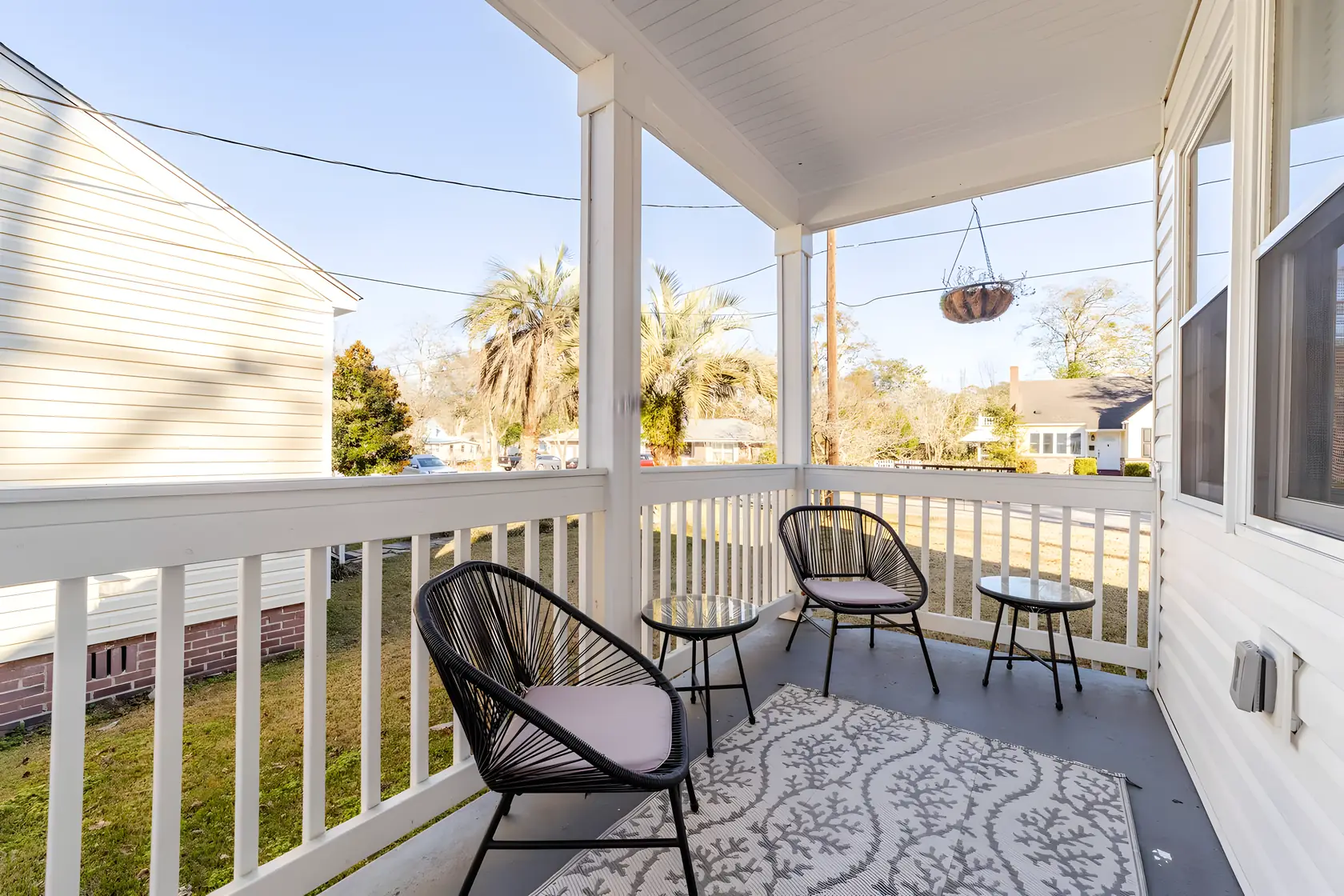 Side porch with rope chairs and a patterned rug, looking over the neighbor gardens