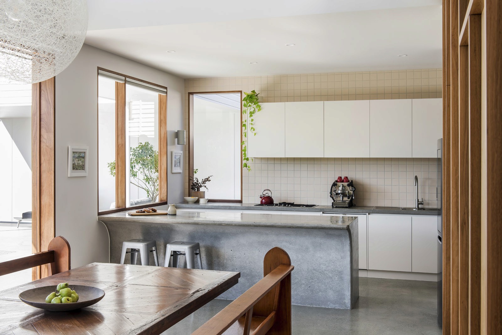 Open-plan kitchen and dining area with concrete island, timber table, and natural light from large windows
