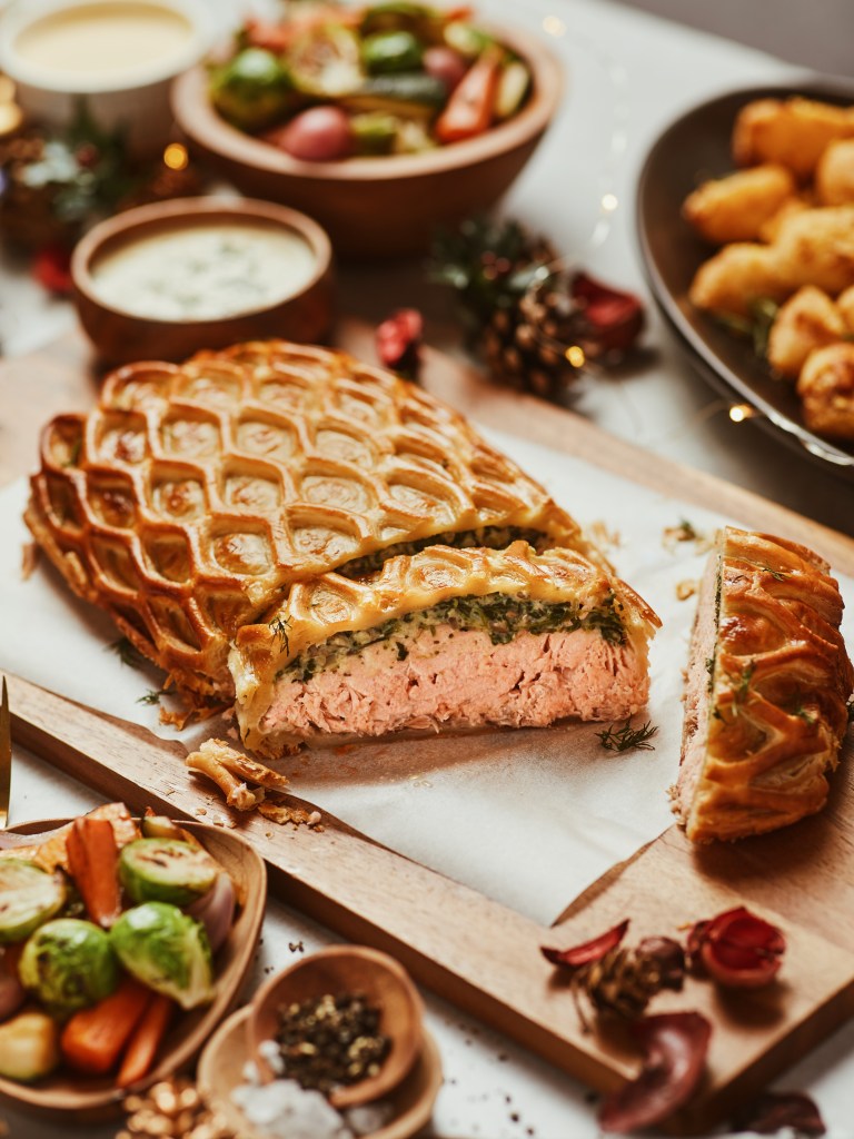 A beautifully arranged Christmas feast showcasing a sliced savory dish on a wooden board, surrounded by bowls of fresh salad, dipping sauces, and garnished herbs, decorated for the holiday season.