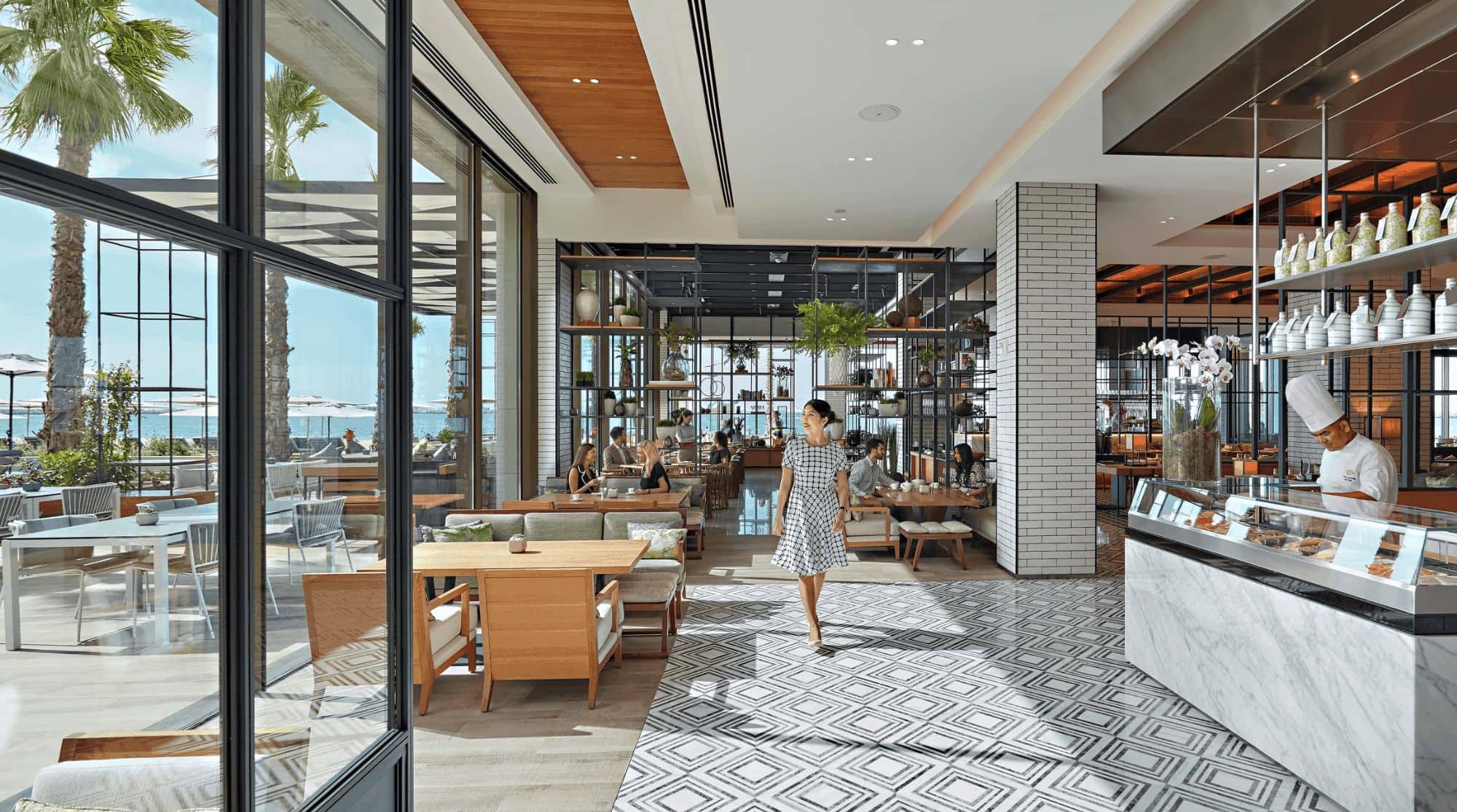 A modern beachfront restaurant with large windows, open kitchen views, modern seating, and seaside views. 