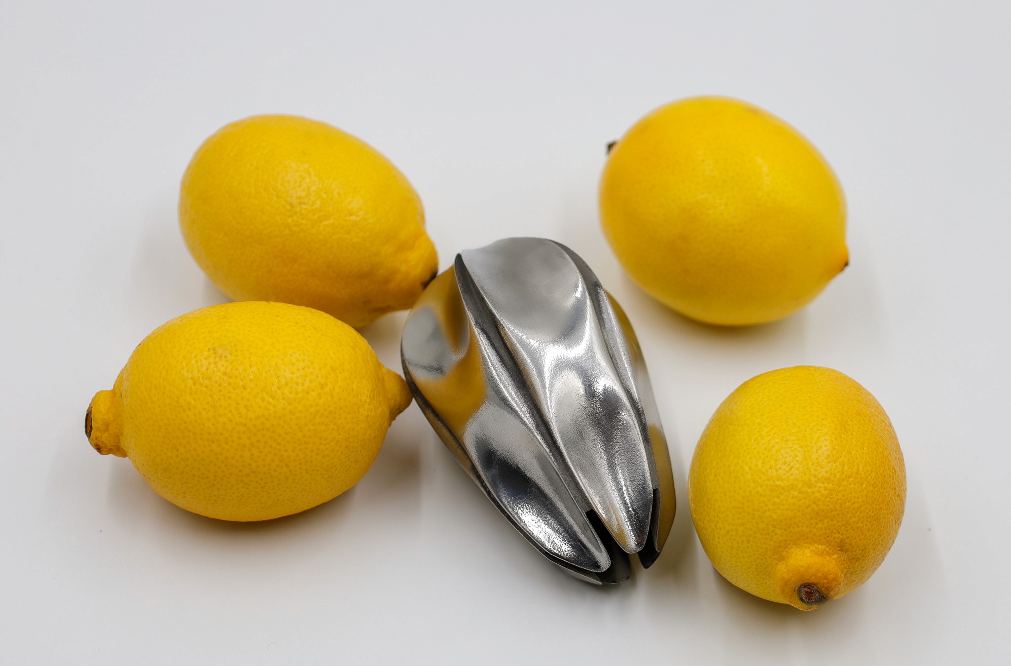 Four fresh lemons arranged around a metal lemon squeezer on a white background.