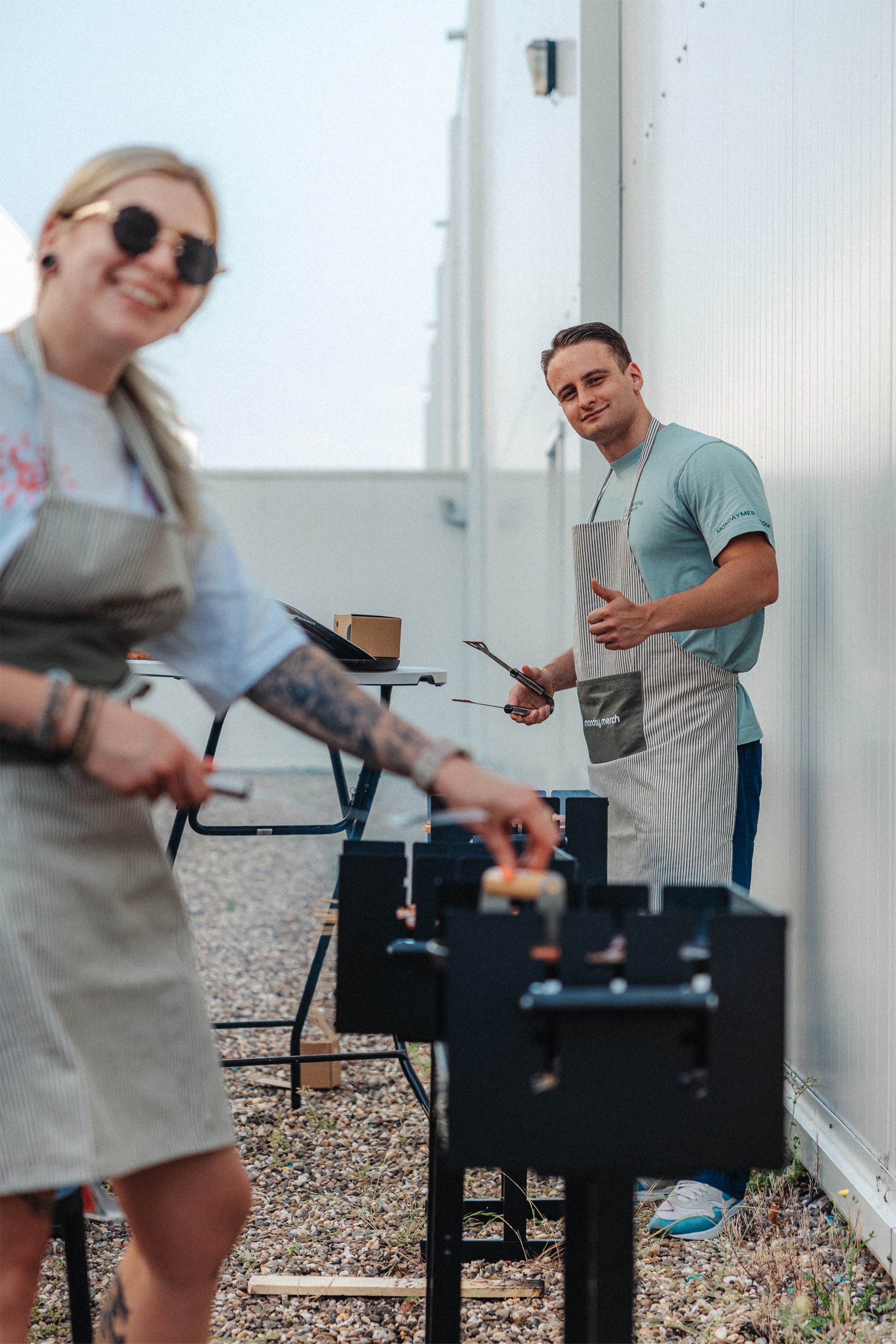 A person with long blonde hair smiles and waves in front of a purple background, holding a tablet.