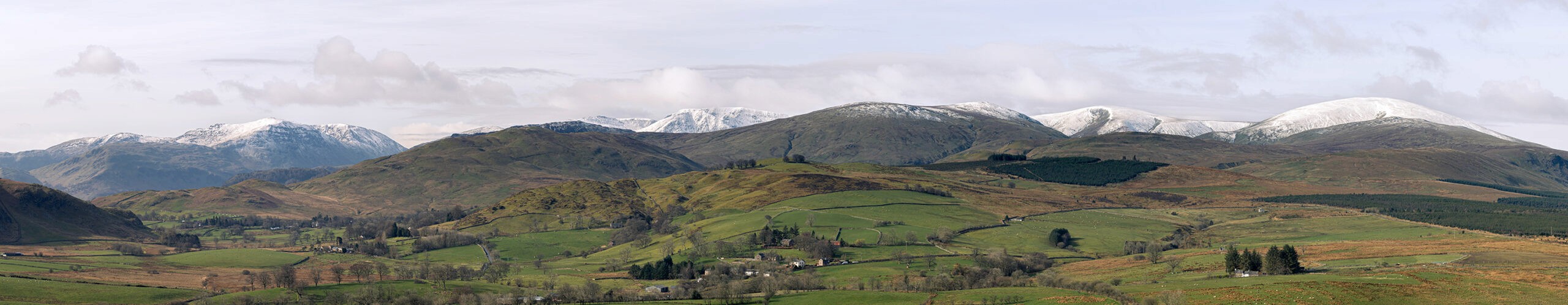 A super-wide pano from halfway up Great Mell Fell. It shows the wide mountain range, some covered with snow.