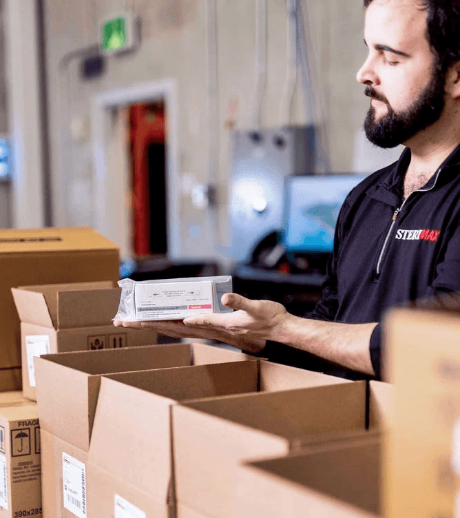 A SteriMax team member carefully inspecting a packaged pharmaceutical product in a distribution warehouse.