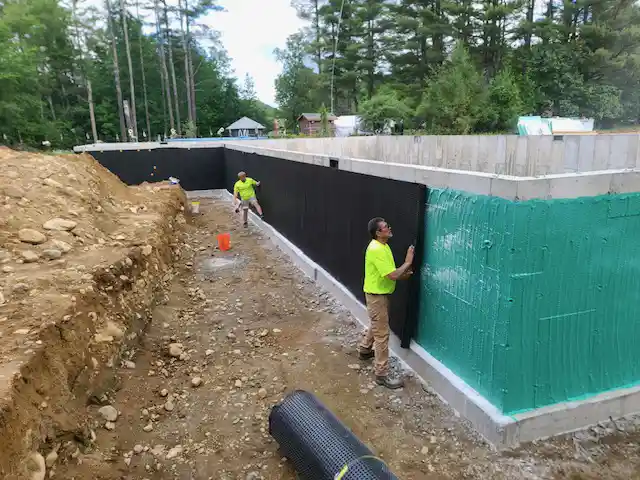 Waterproofing applicators placing Rub-R-Board drainage board easily on a new home foundation