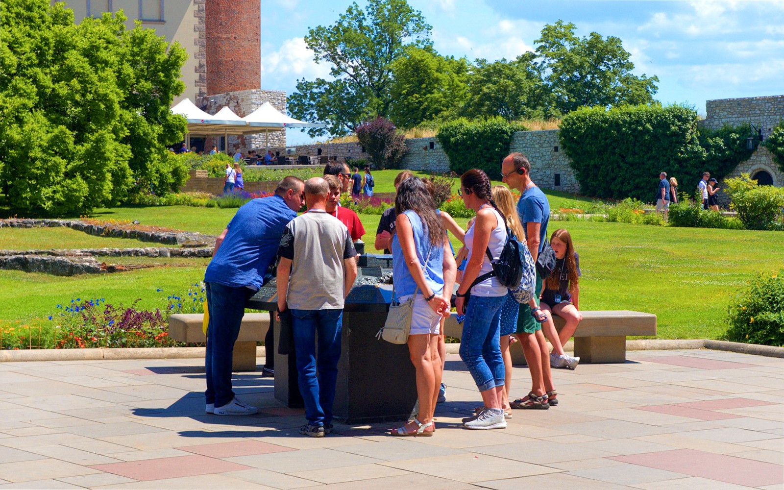 Tourists examining a miniature model of Wawel Royal Castle in a garden setting.