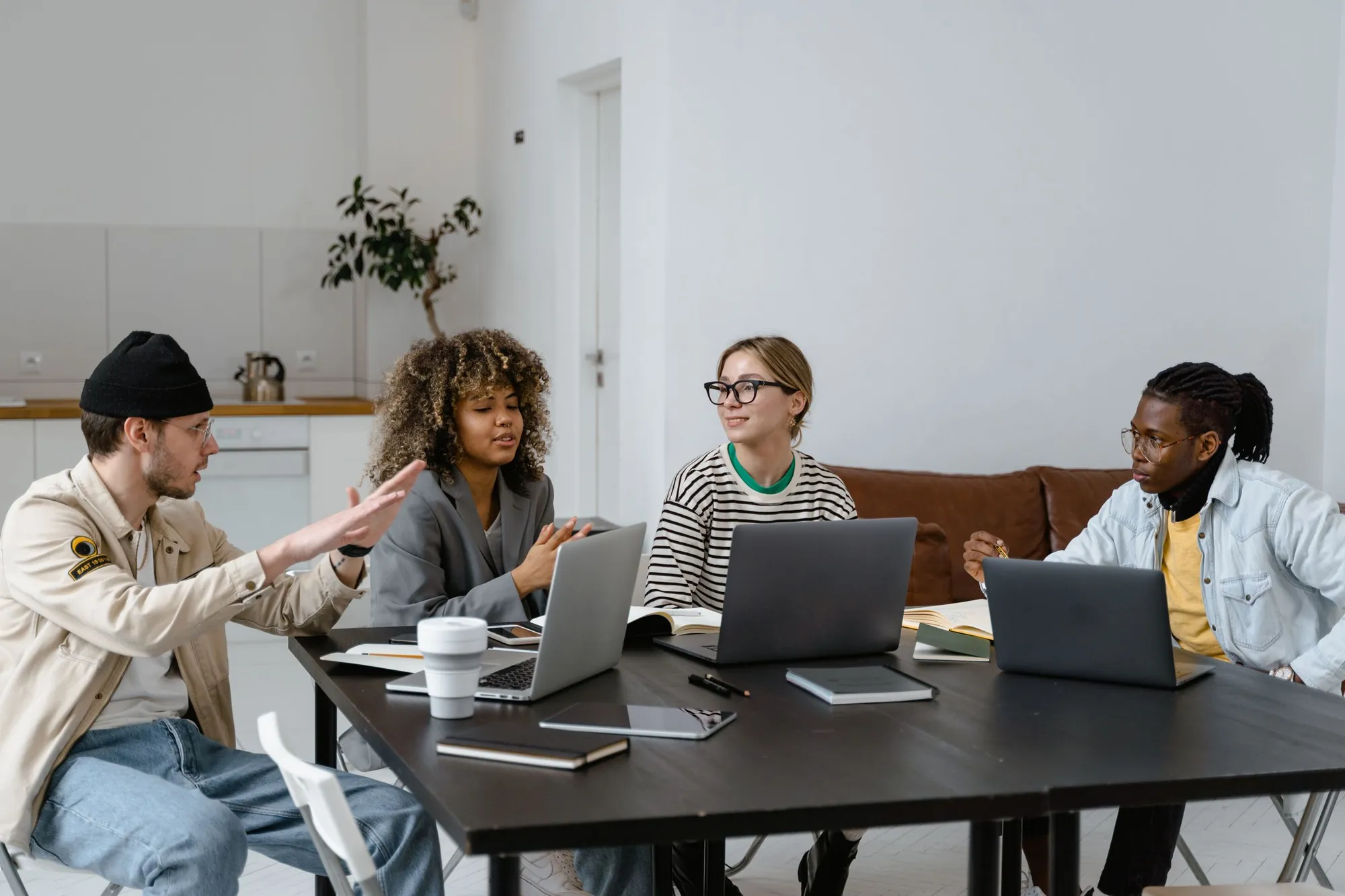 Four colleagues talking around a table of laptops in a bright office