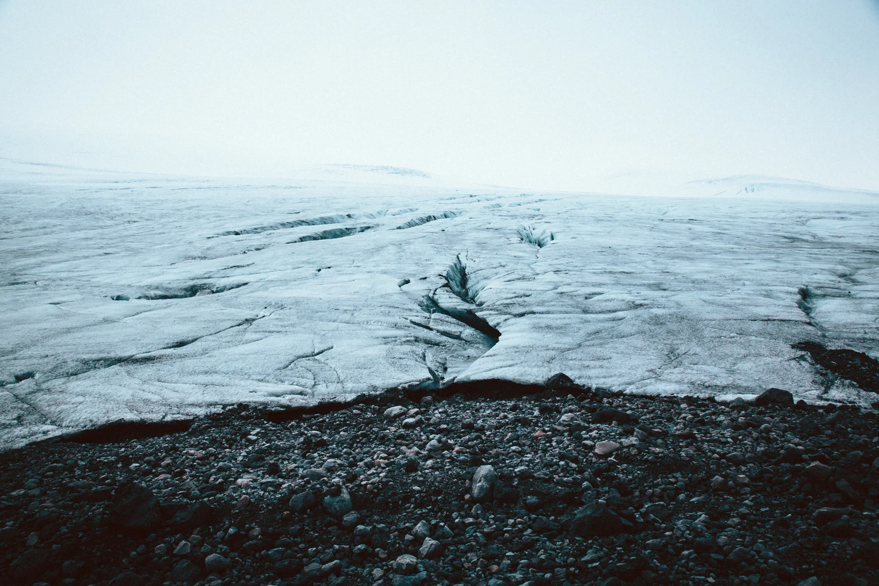 A crevassed glacier surface running to a flat white horizon