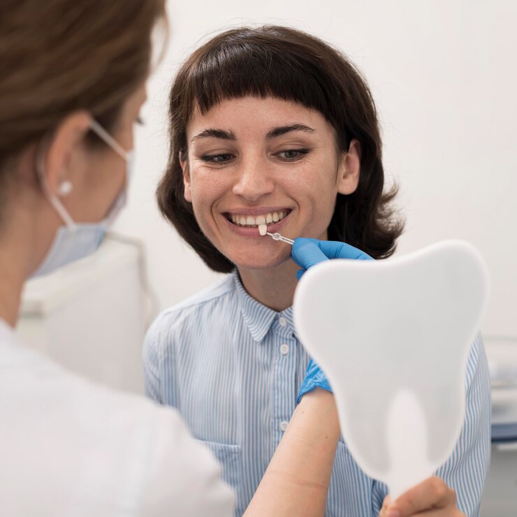 A female patient holding a dental mirror, smiling and examining her teeth with the help of a dentist.