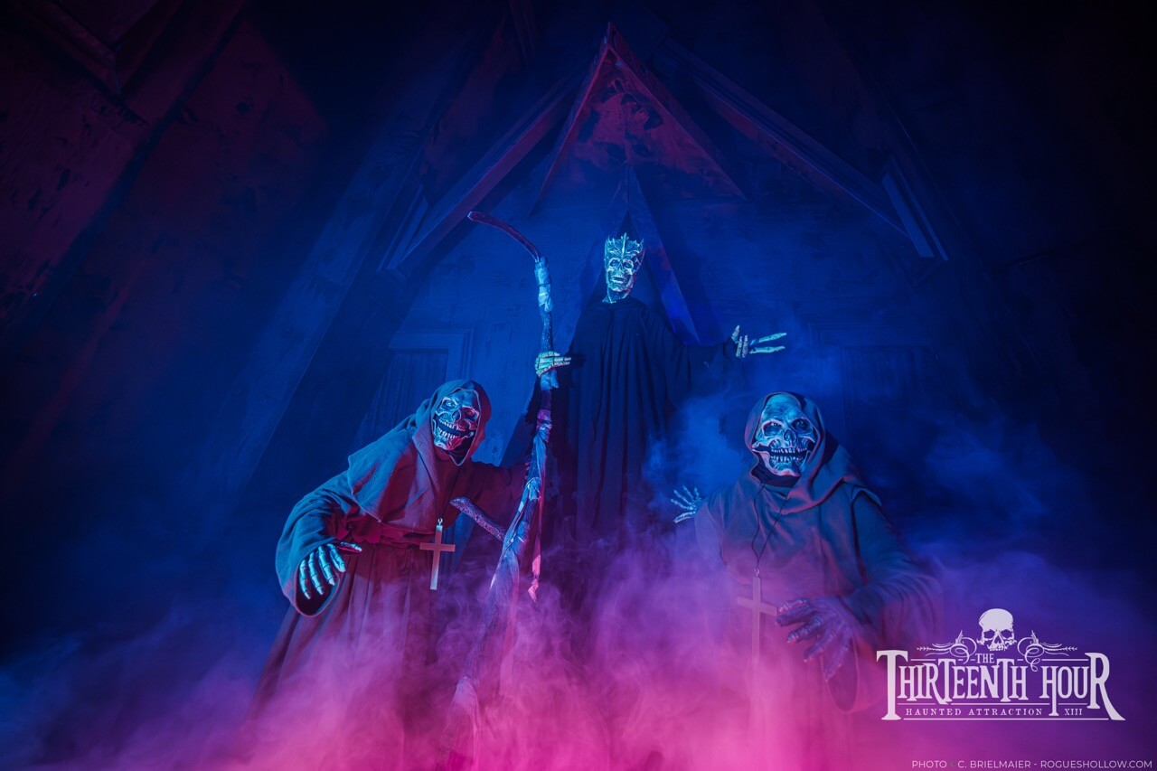 Three skeletal-robed scare actors standing in blue and magenta fog