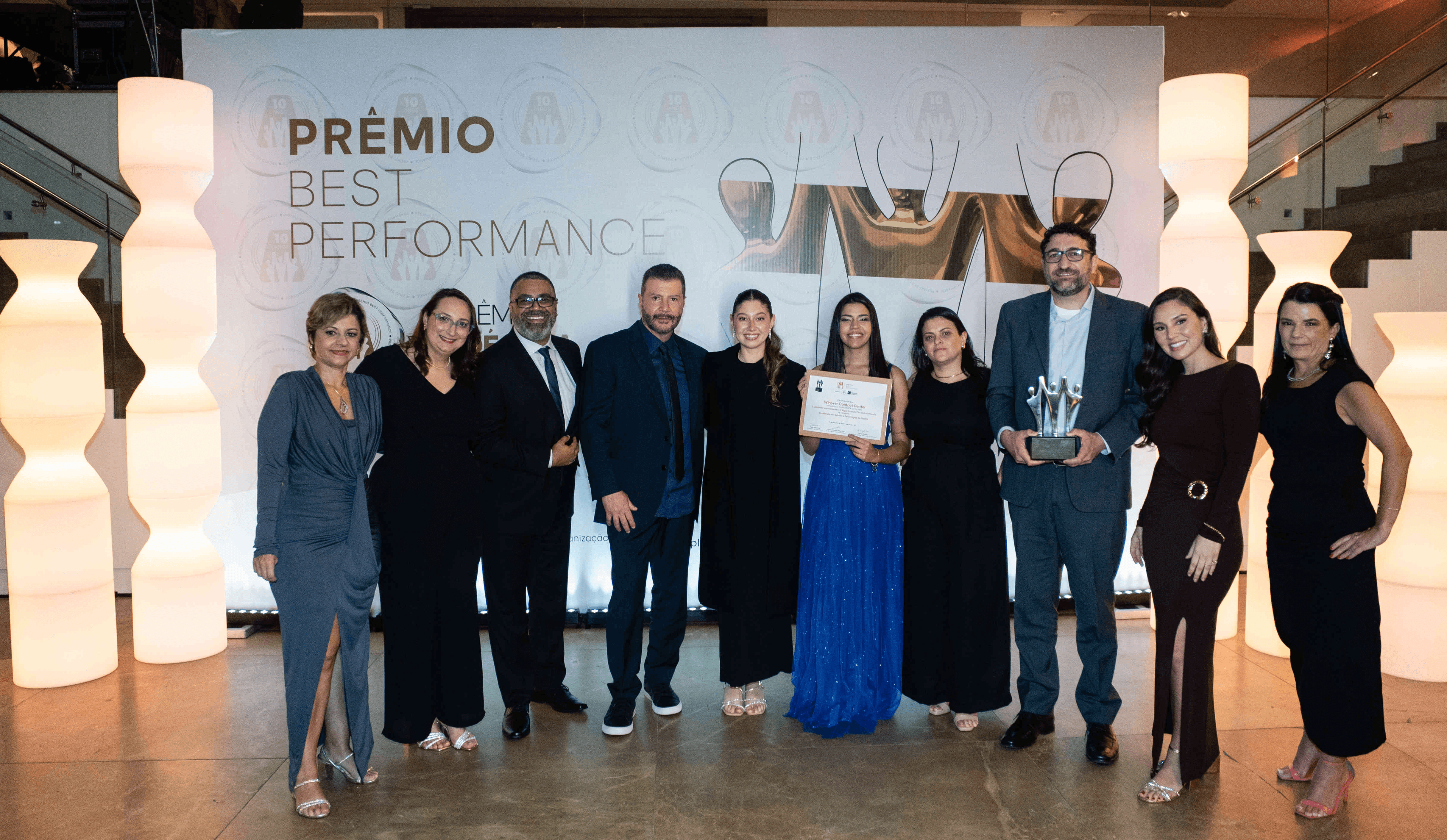 Executivos da Winover Contact Center posando com troféu prata e certificado no palco do Prêmio Best Performance 2025