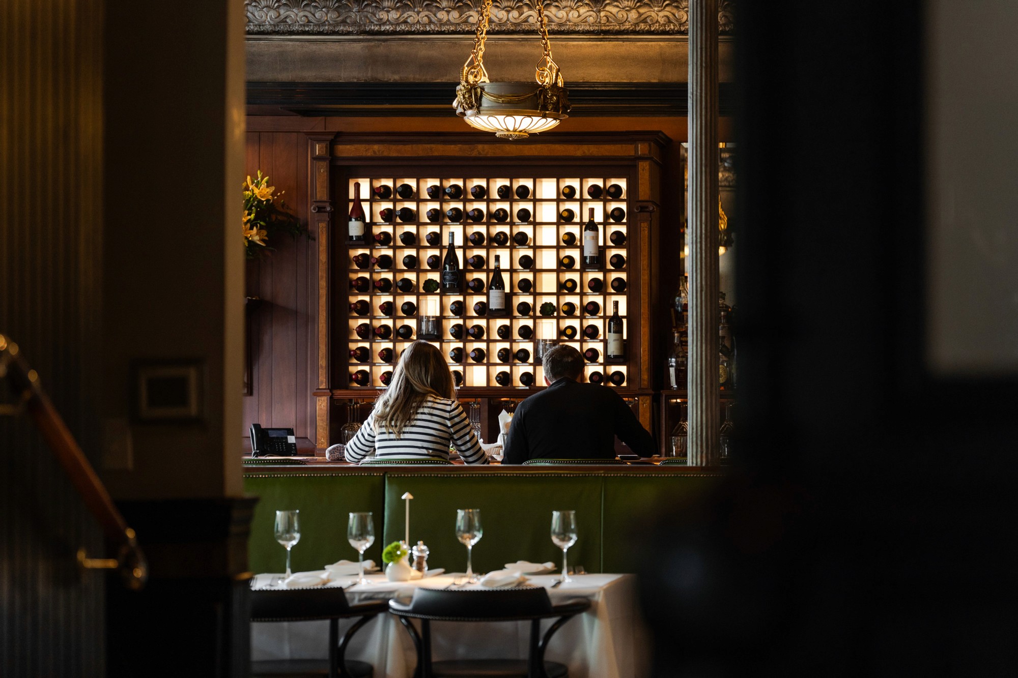 Two guests at a table in front of a lit wine wall at Lindey's