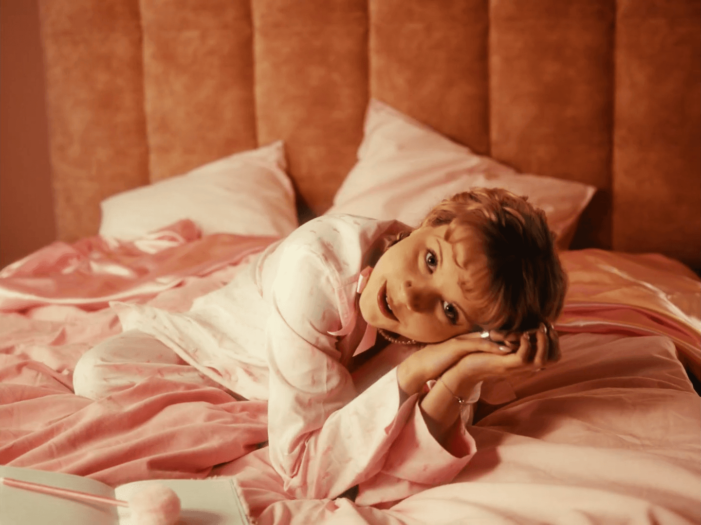 woman lady lying on pink bed cinematic looking at camera singer finnish