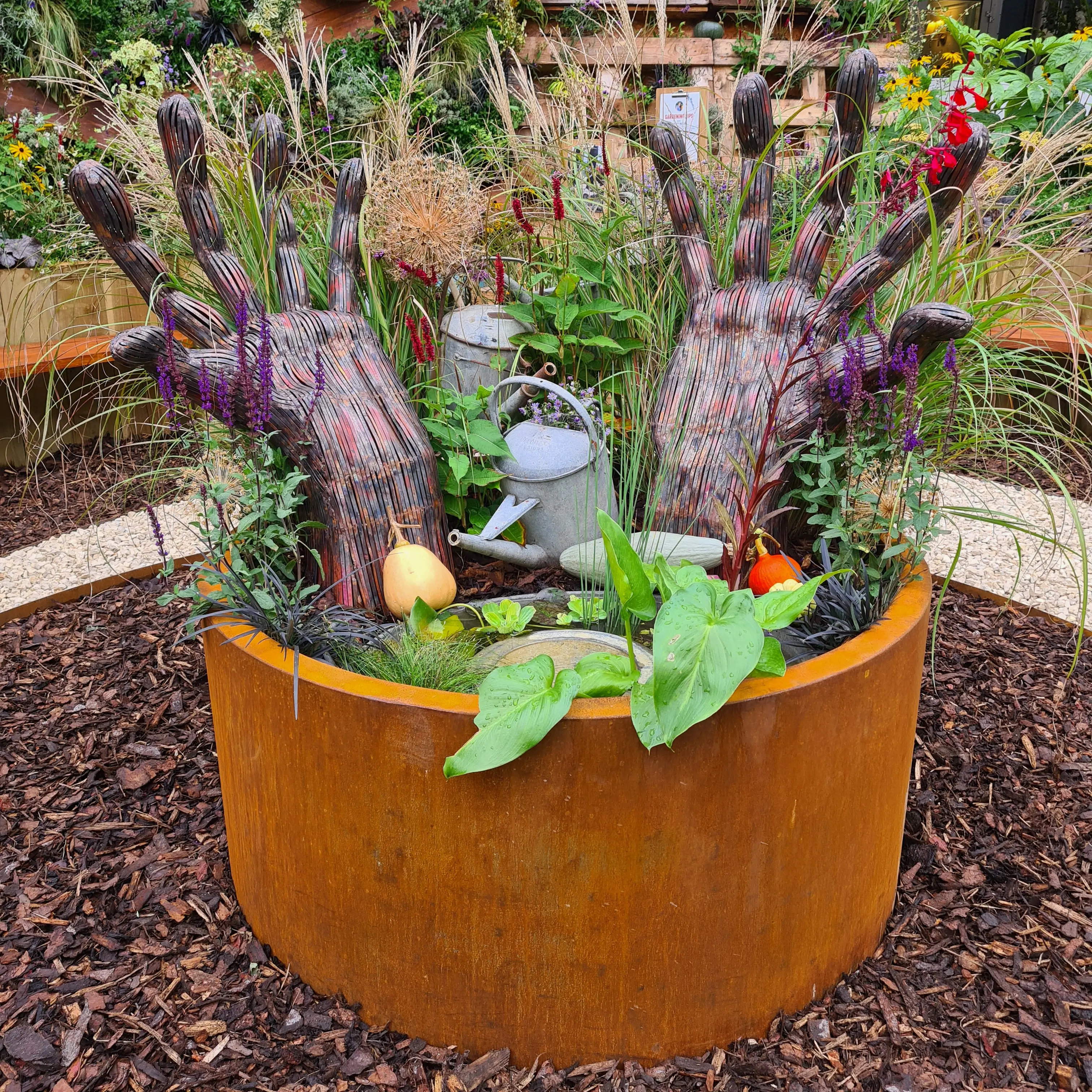 A metal planter filled with various plants, including colorful succulents and leafy greens, in a garden setting.