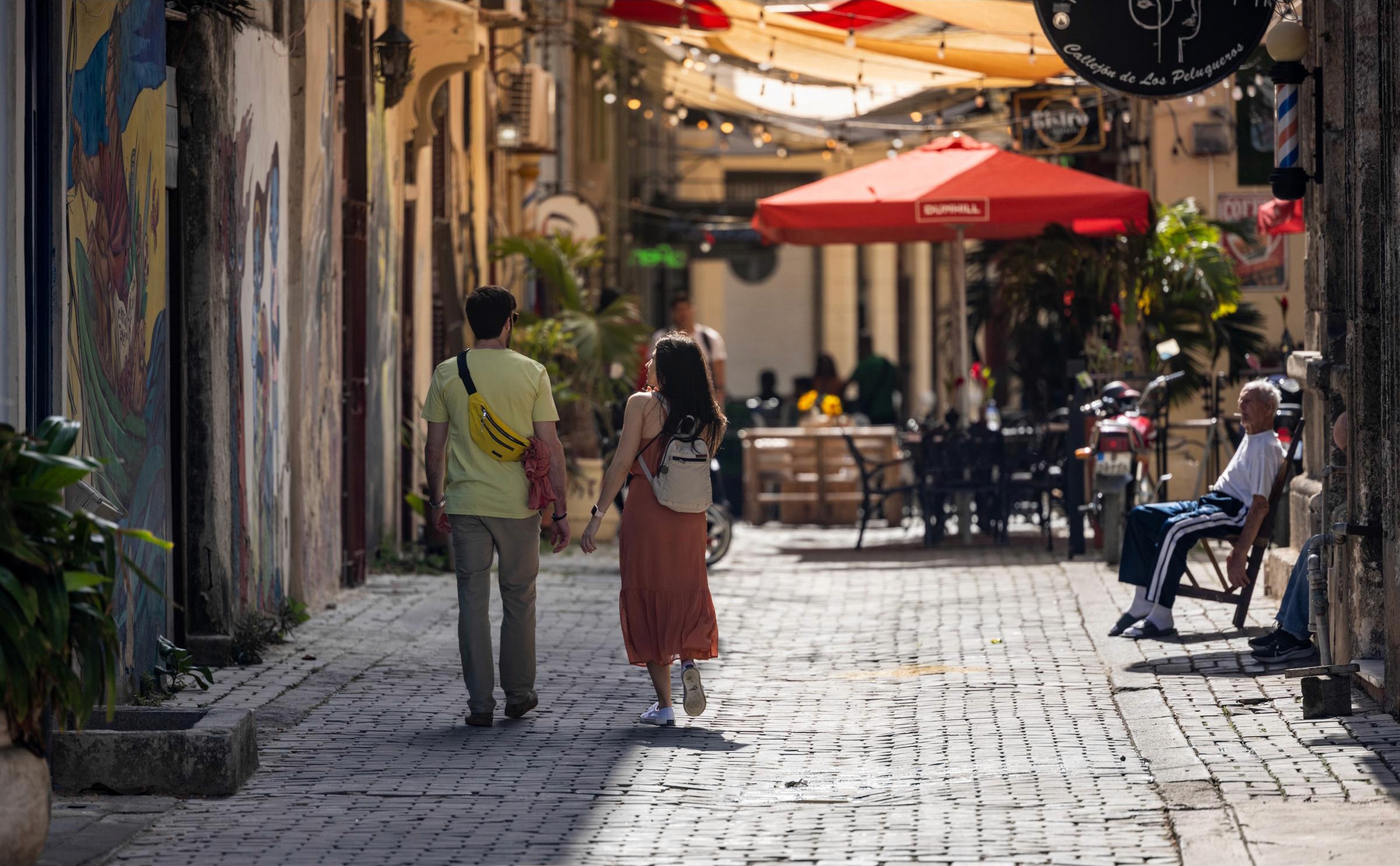 Couple Walking the Streets of Havana, A Local Relaxes in his Chair