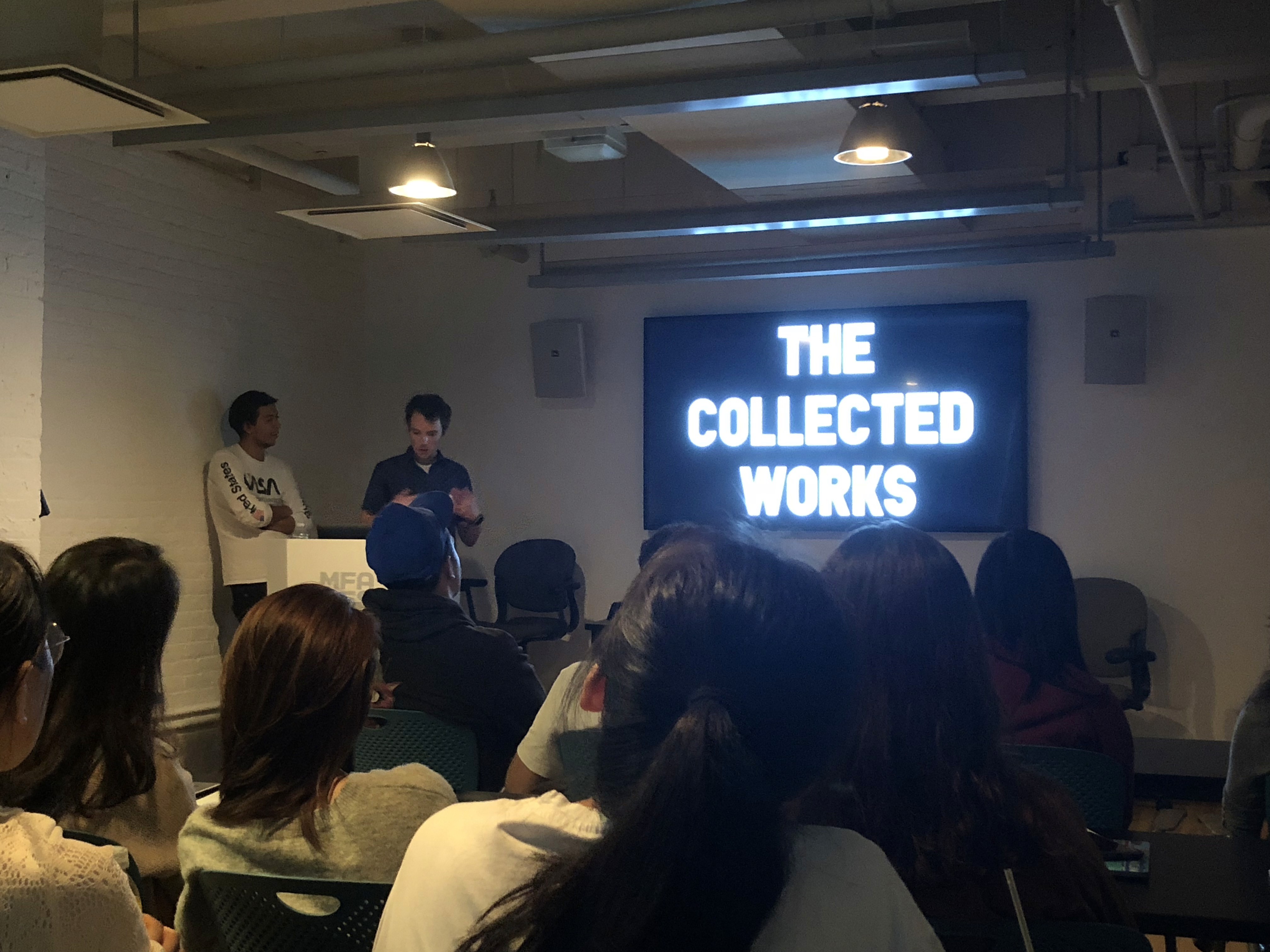 Students in a classroom watching a monitor that shows: The collected works.