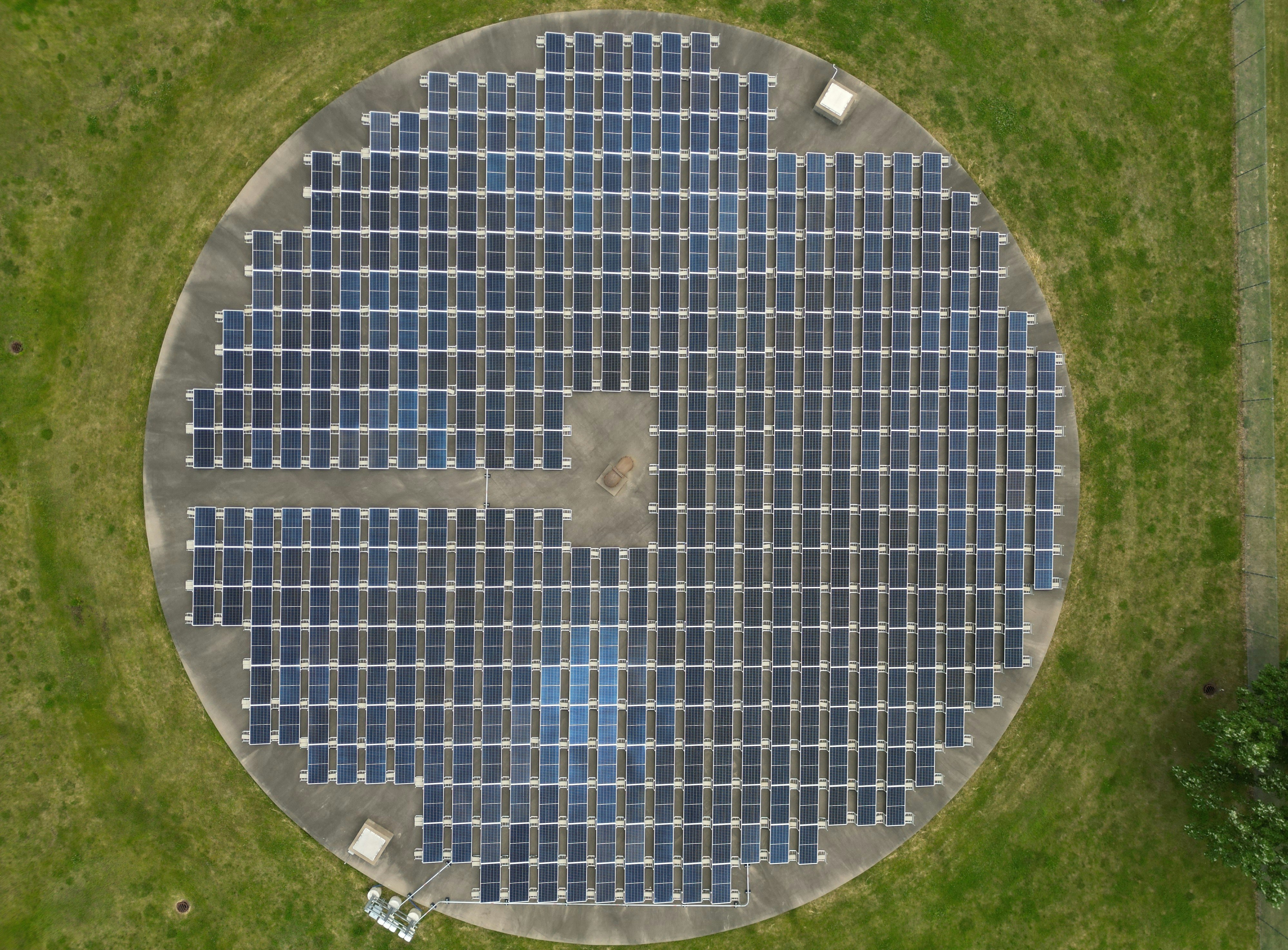 Aerial view of a circular solar panel array on grass.