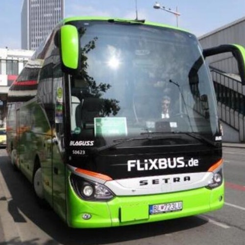 Un FlixBus verde estacionado en una calle de la ciudad con edificios de fondo. Se puede ver al conductor a través del parabrisas.