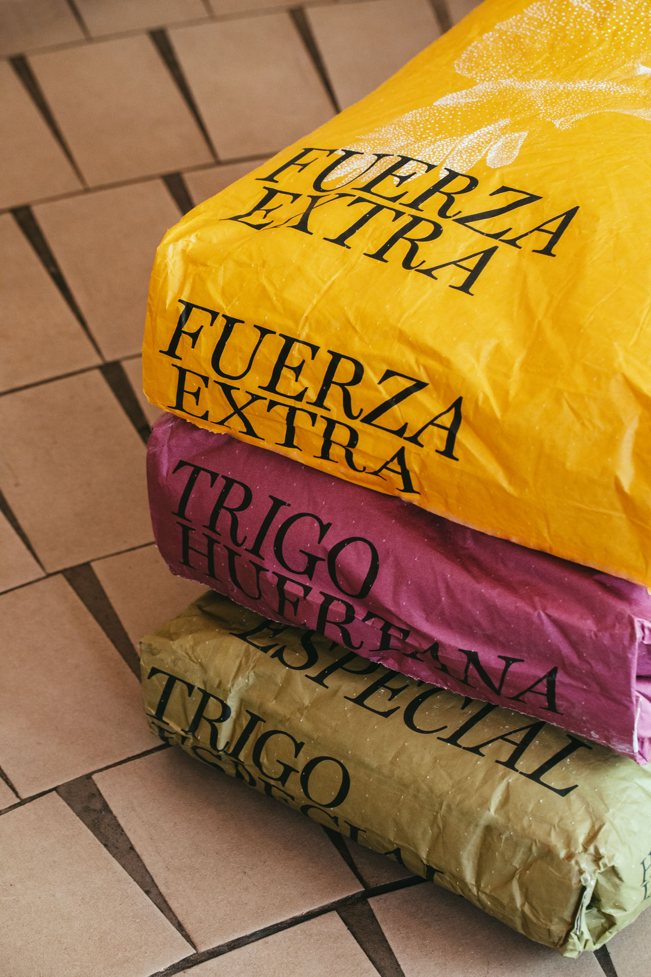 Stacked flour sacks labeled Fuerza Extra and Trigo Especial on a bakery tiled floor.