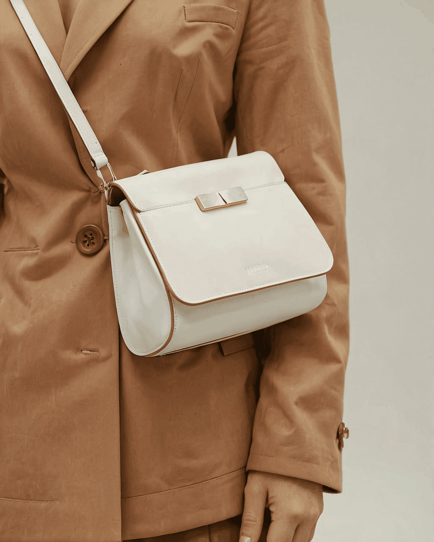 Person wearing beige coat holding minimalist white leather handbag