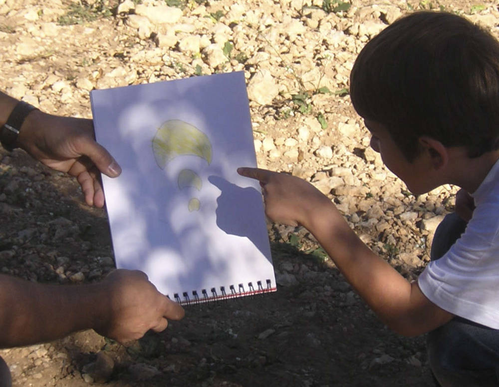 Two people point at a paper on the ground, showcasing a drawing of clouds against a blue background.
