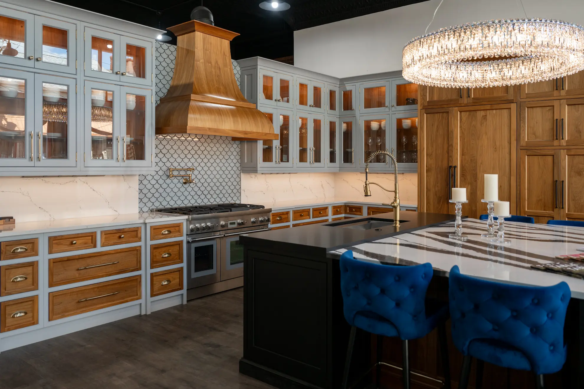 Inside the Haute Designs kitchen and bath showroom in Zelienople, PA — powder-blue cabinetry, a brass range hood, and a marble island beneath a crystal chandelier