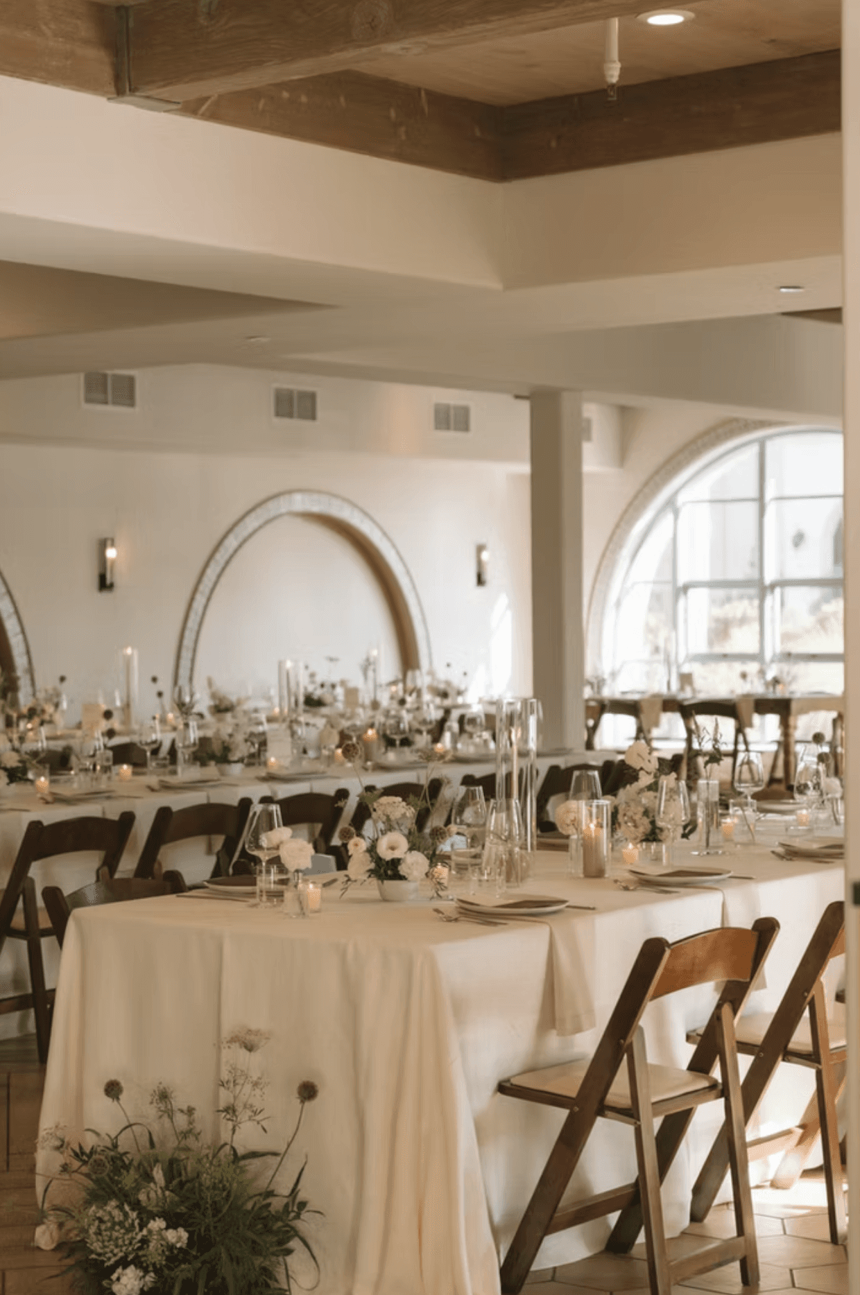 A beautifully set dining table with white tablecloth, cutlery, and fresh greenery in a cozy, well-lit space.