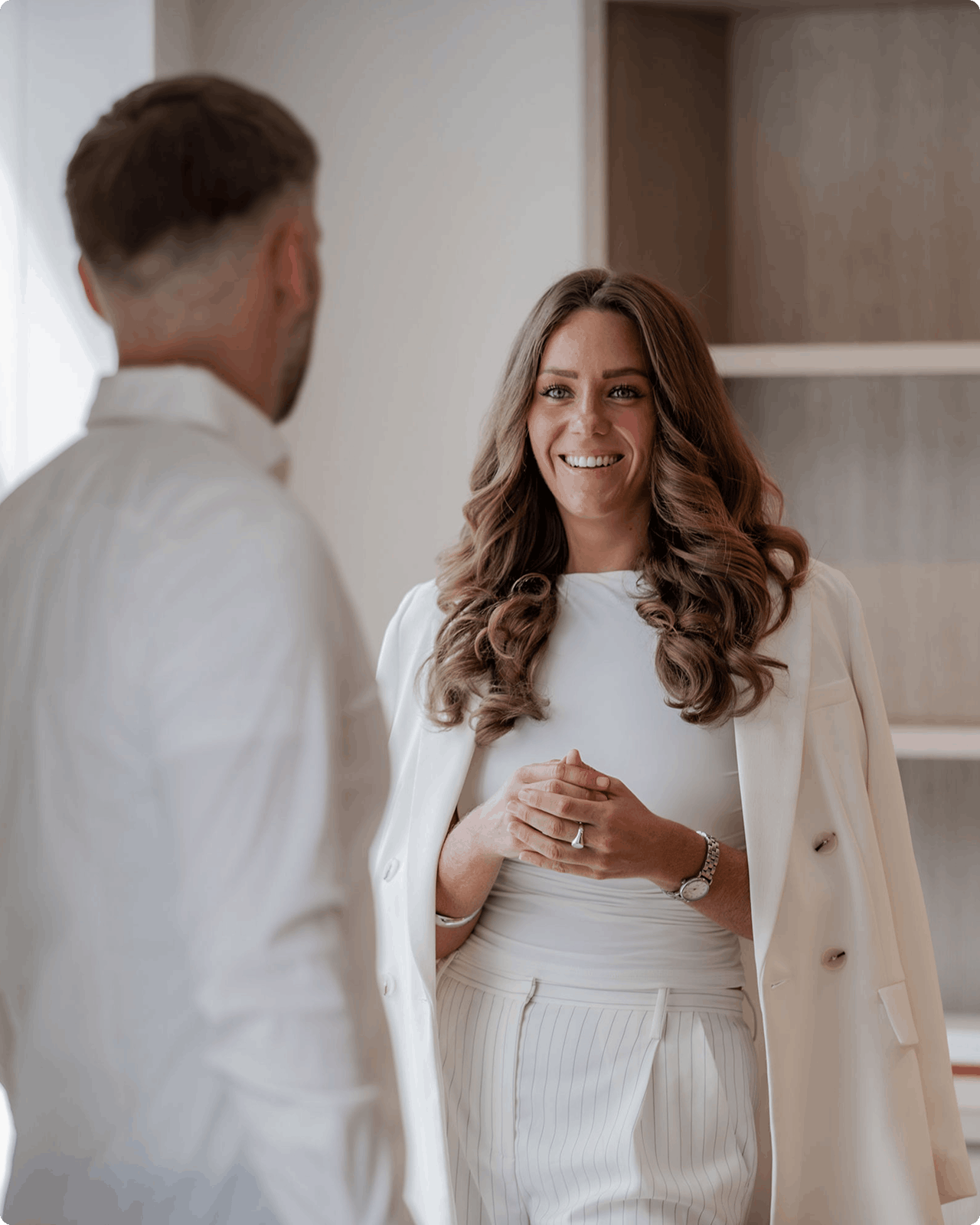 Smiling woman in white blazer with long wavy hair looks at camera.