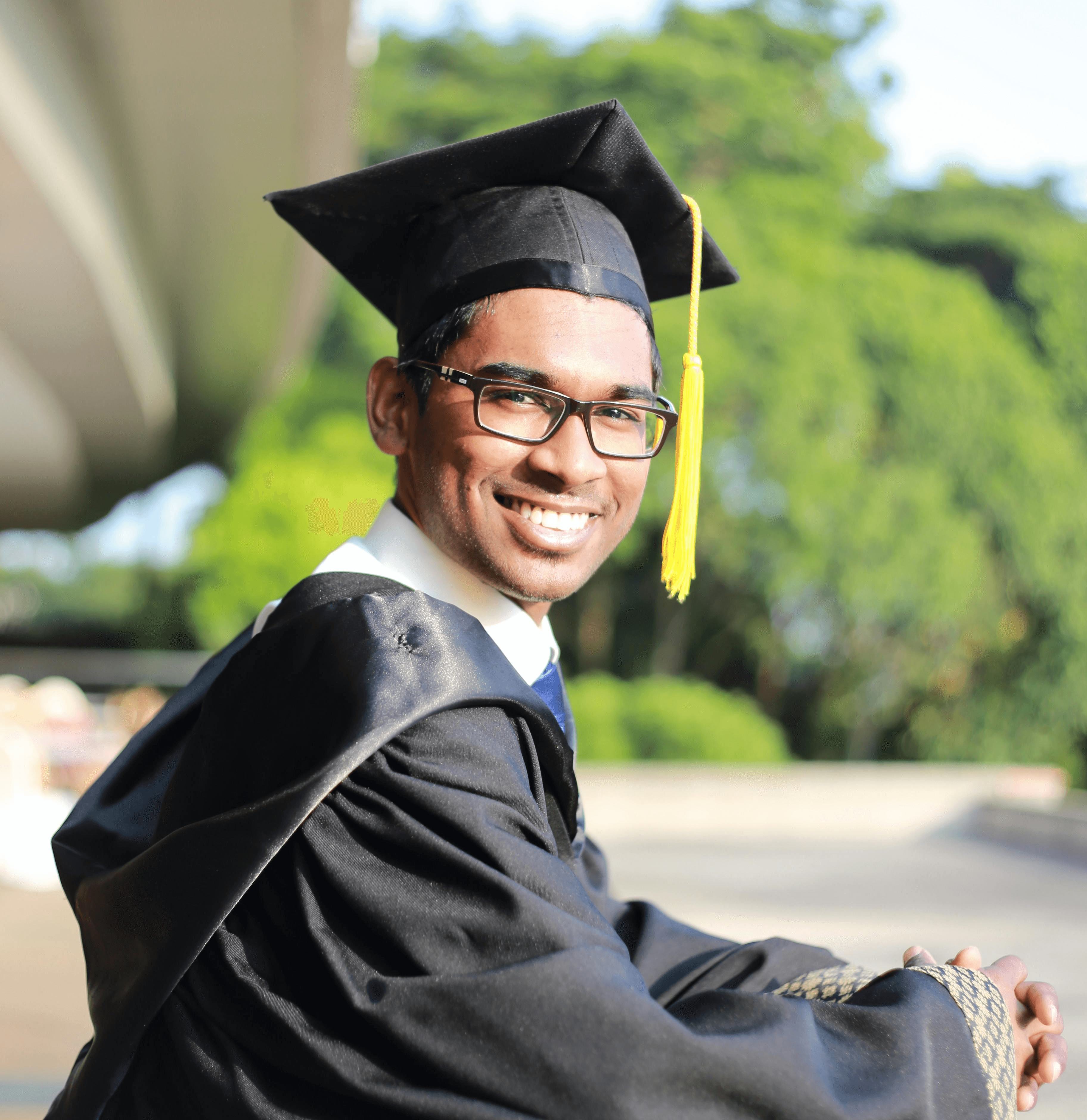 Smiling young man in graduation cap and gown standing outdoors, celebrating academic achievement and success on graduation day.