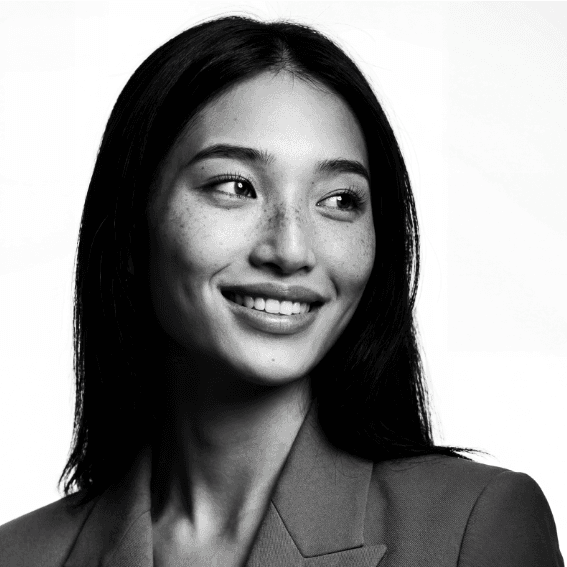 Portrait of a woman with long, smooth hair swept to the side, in a suit, on a plain background.