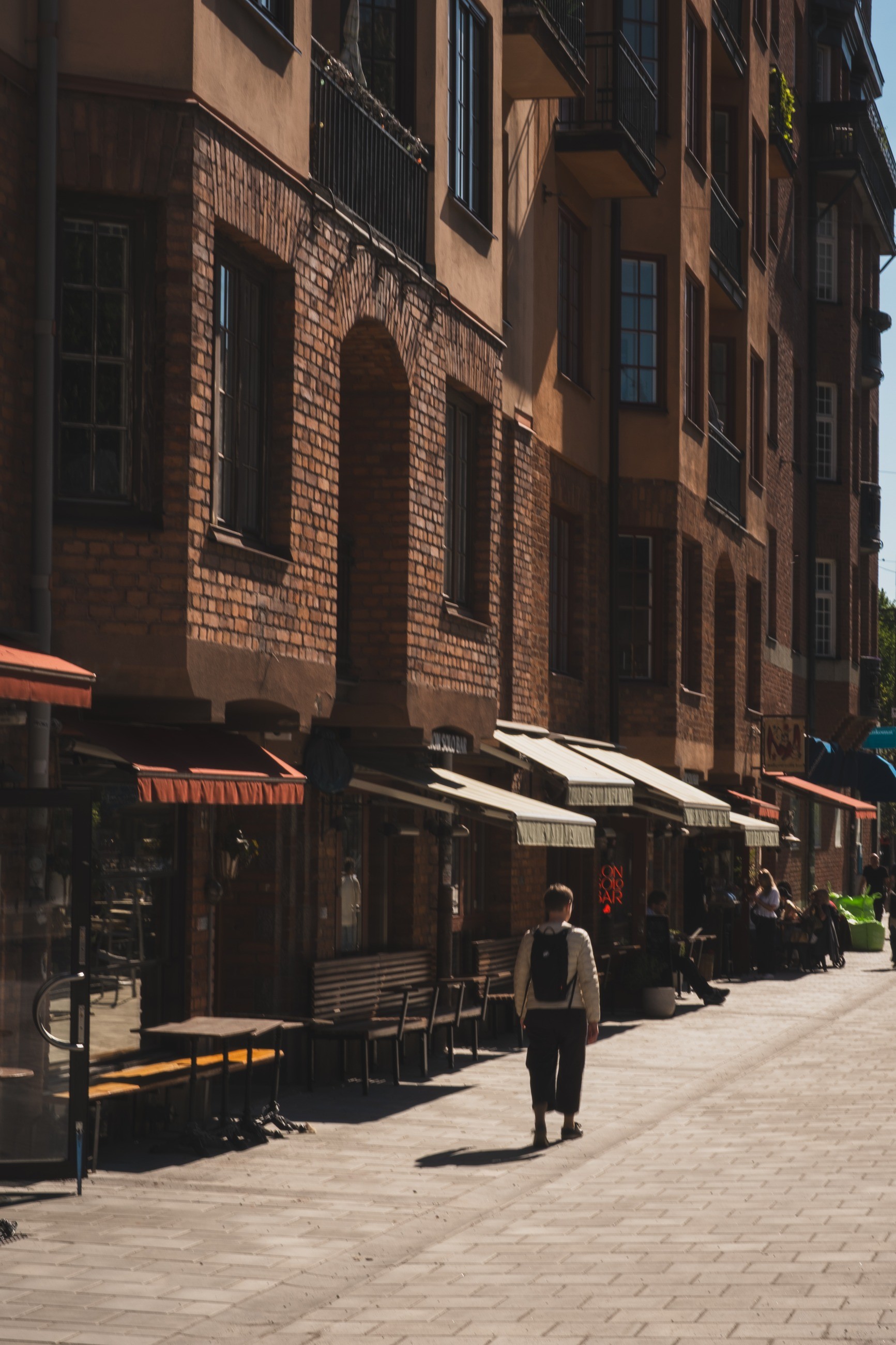 A pedestrian crossing a narrow Stockholm street between light and shadow