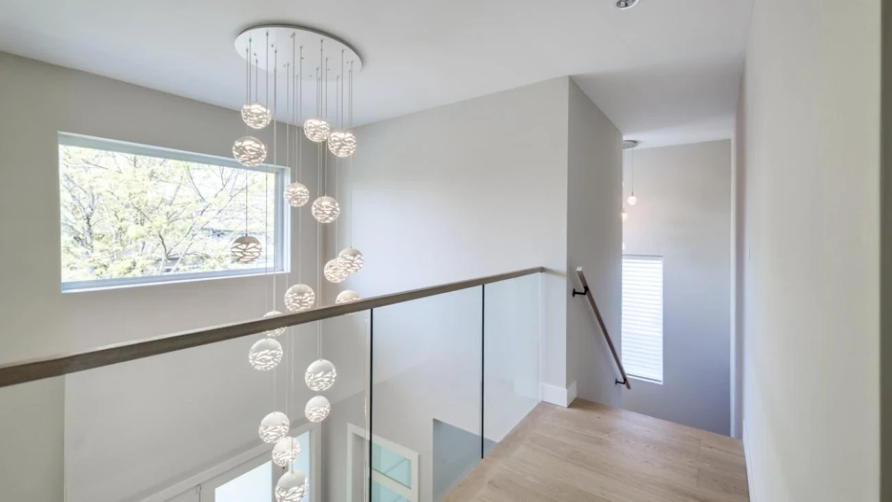 Stunning modern staircase with glass railing, light wood treads, and dramatic cascading sphere pendant light fixture in two-story foyer