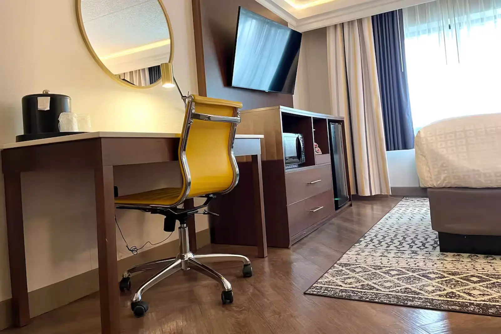 Modern hotel room with a desk, bright yellow chair, and wall-mounted TV.
