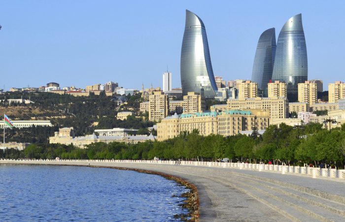 Dirt road flanked by vineyards and cypress trees, rolling hills, mist, and distant town in Tuscany.
