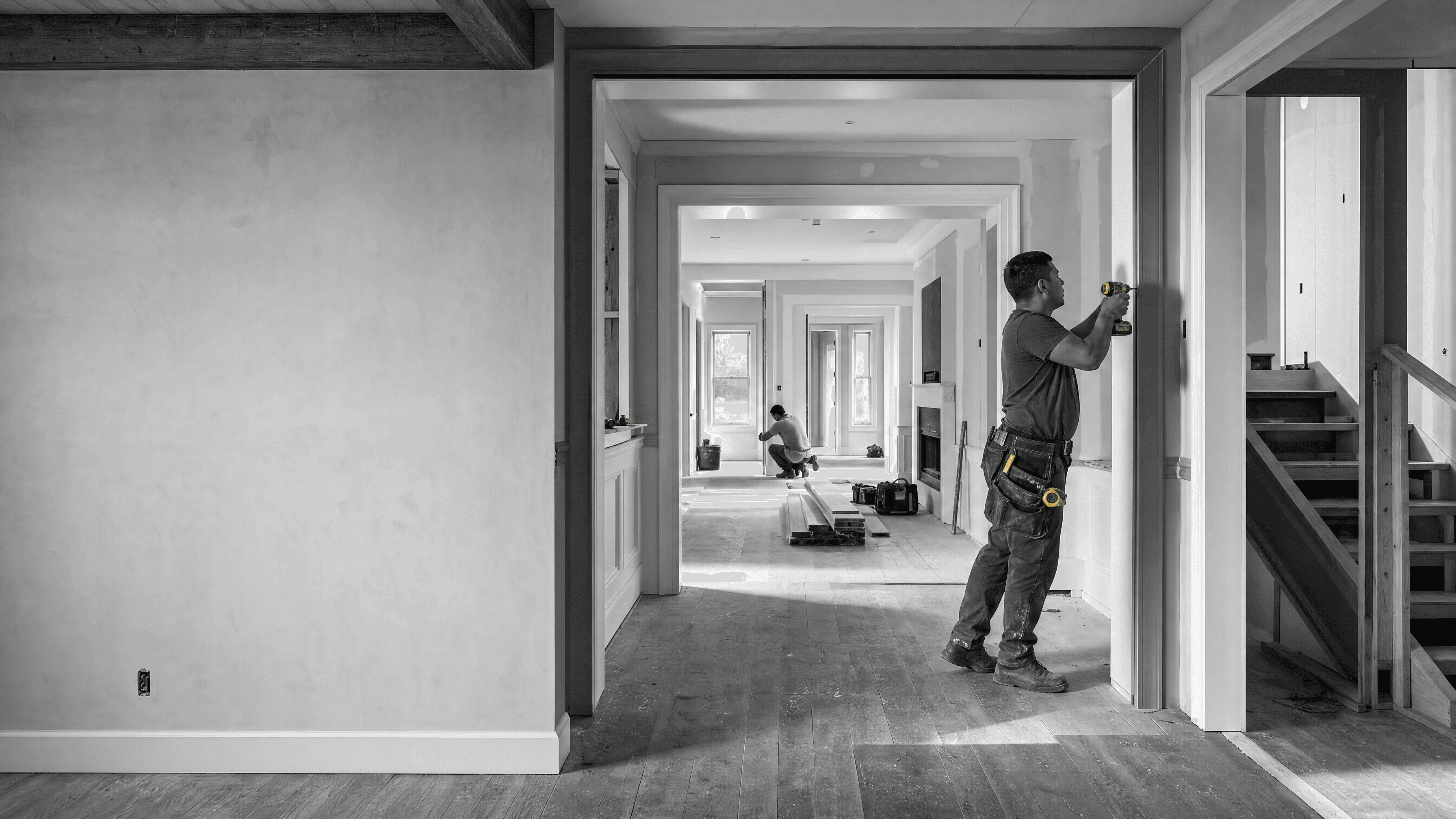 Two workers install interior finishes across connected rooms during a multi-room residential renovation.
