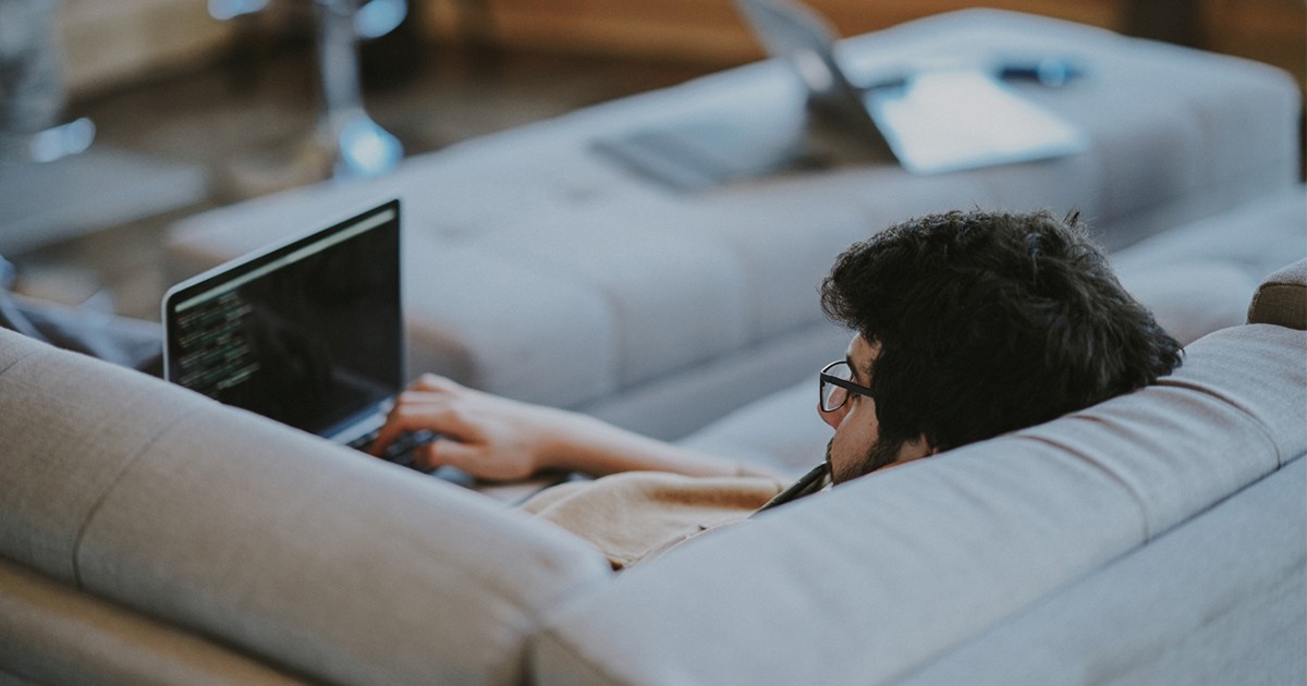 Person lying down on a sofa working on their laptop