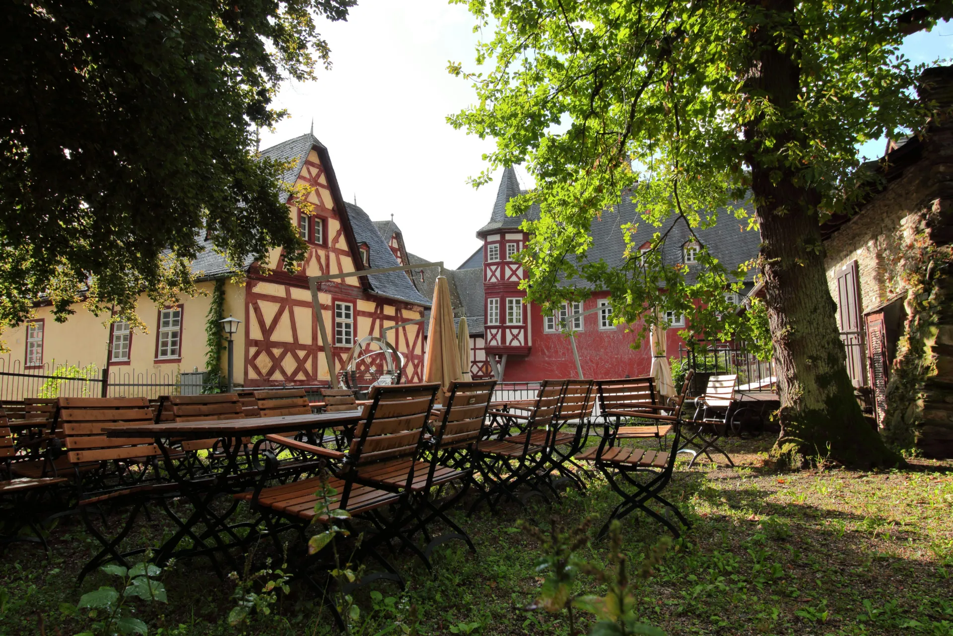 Ein Vorhof umgeben von drei großen Fachwerkhäusern. Im Vordergrund ist eine kleine Sitzgelegenheit mit einem großen Tisch und Stühlen drumherum.