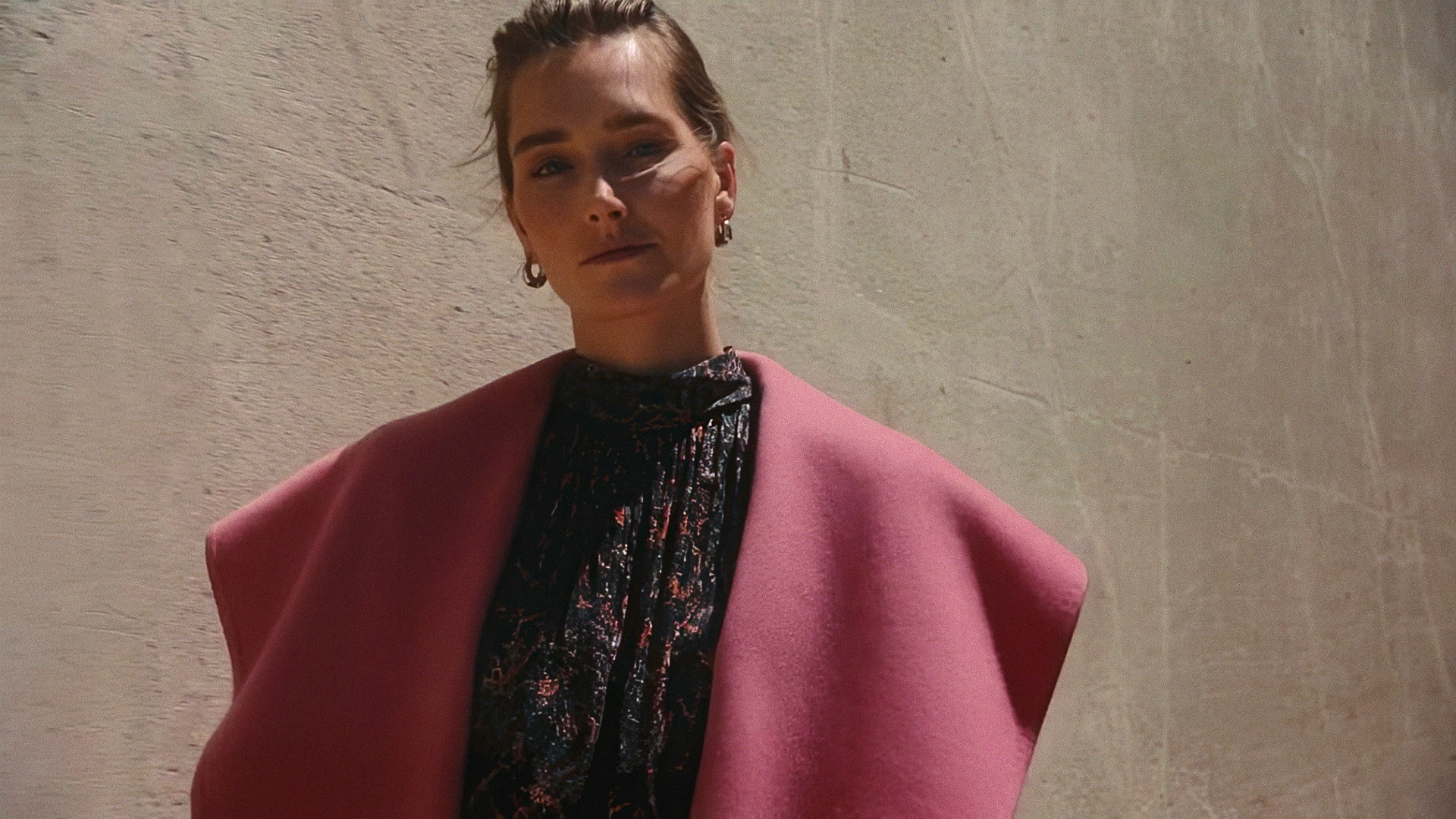 Close-up of a woman in a pink coat over a black printed dress against concrete, Lafayette 148 New York