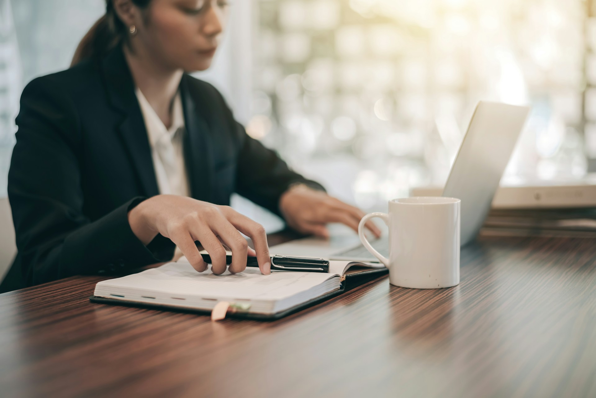 A woman holding a pen while working on a laptop