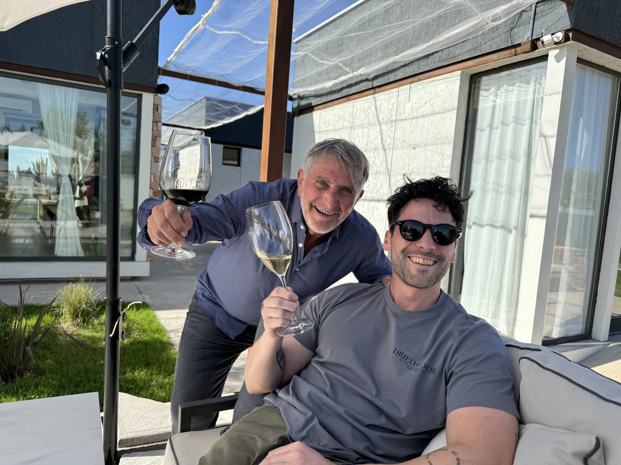 Grazie Mille winery founders Fernando and Leandro raising wine glasses together in La Consulta, Uco Valley, Mendoza, Argentina.