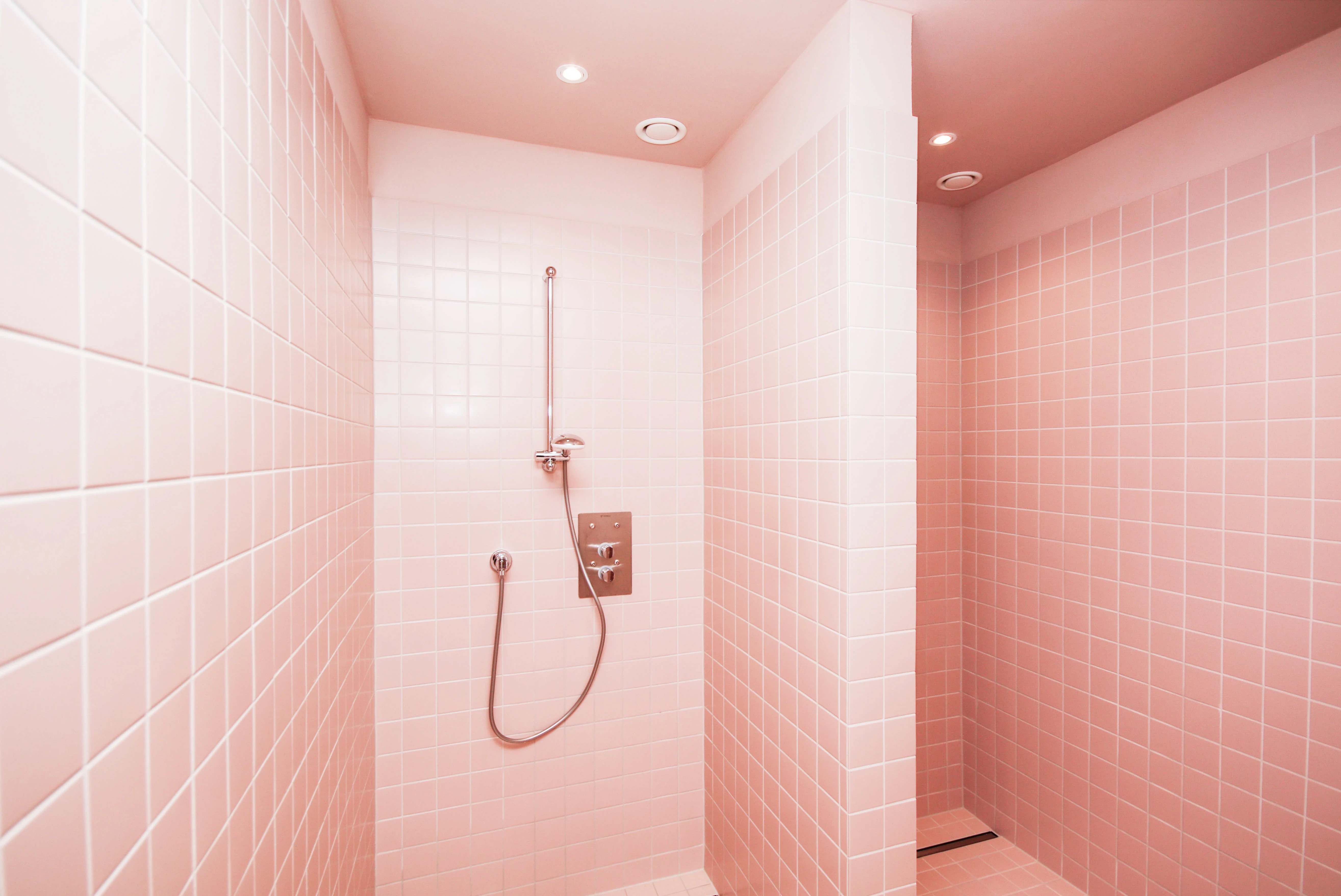 Shower niches at CYCLA tiled completely in soft pink with chrome fittings and recessed ceiling spots.