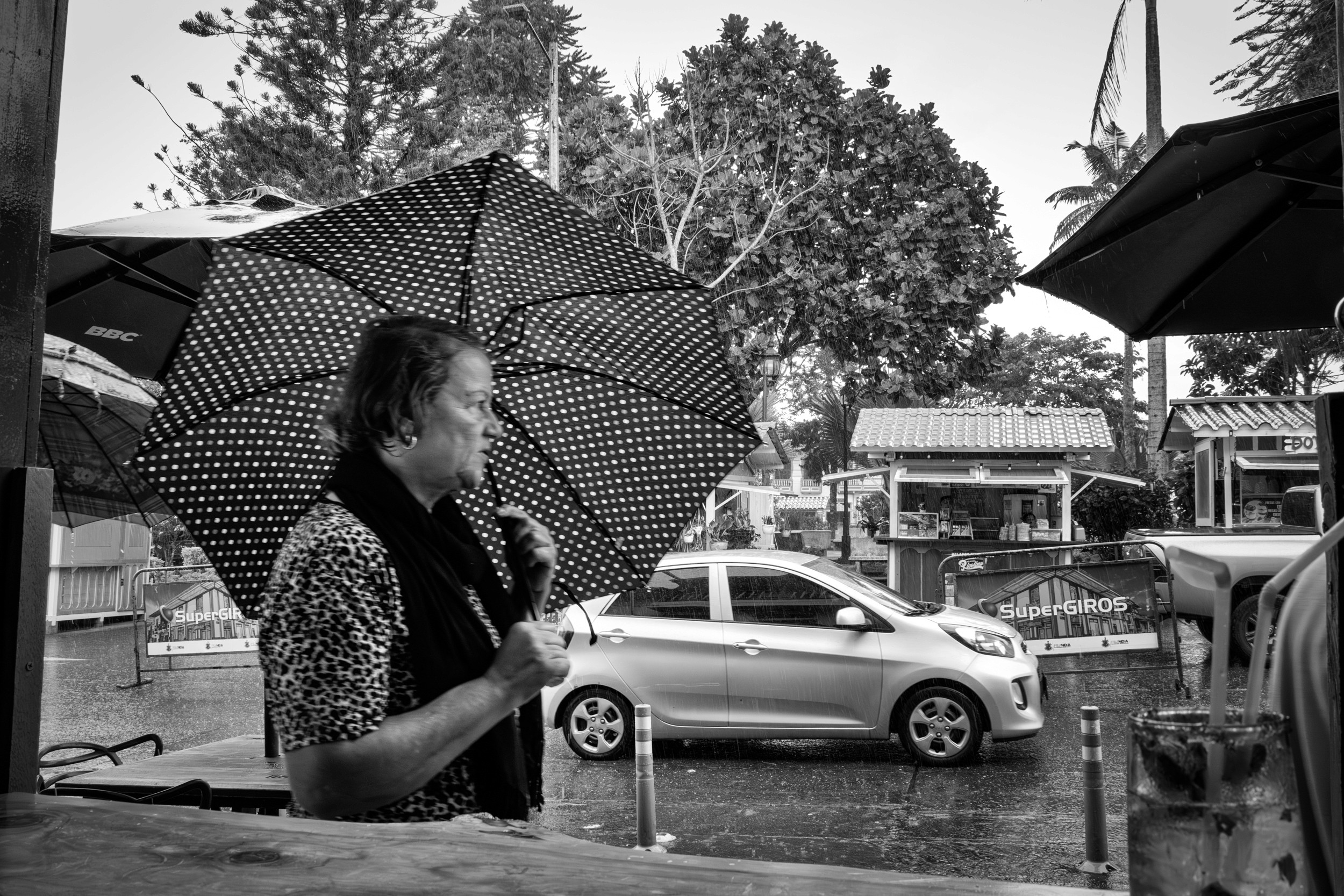 Rainy street scene with people passing by a bar window.
